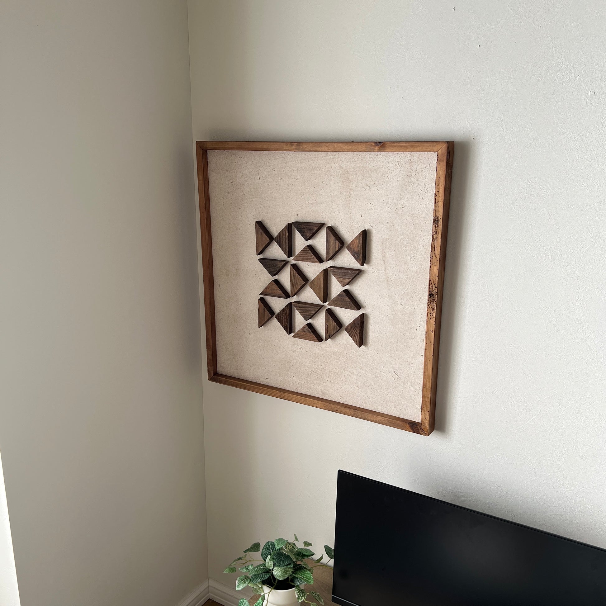 三角形の立体的なウッドパーツが幾何学的に貼り付けられたアートが壁にかかっている様子