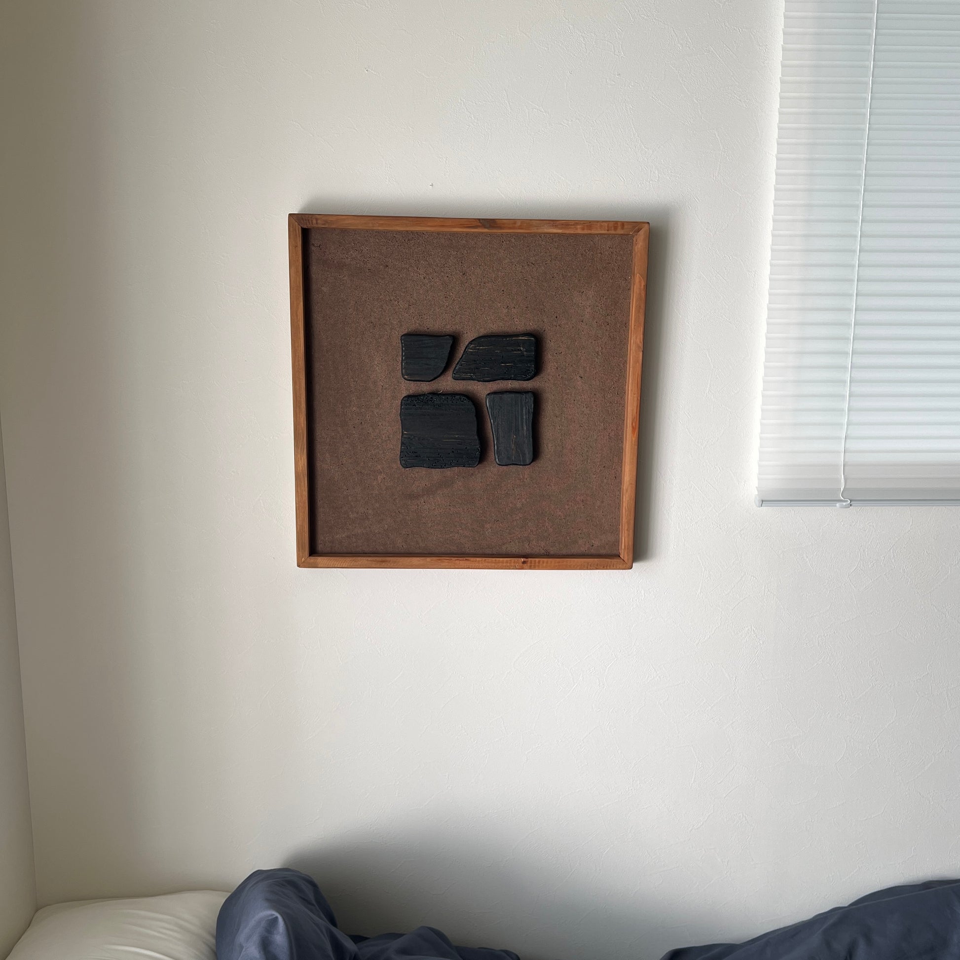 ブラックのウッドピースが立体的に貼り付けられたアートが壁にかかっている様子