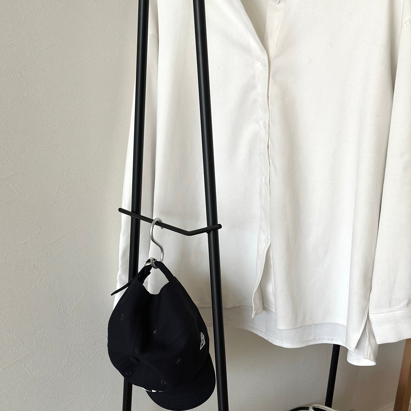 ブラックのスチール製のハンガーラックに洋服や帽子が掛けられている様子
