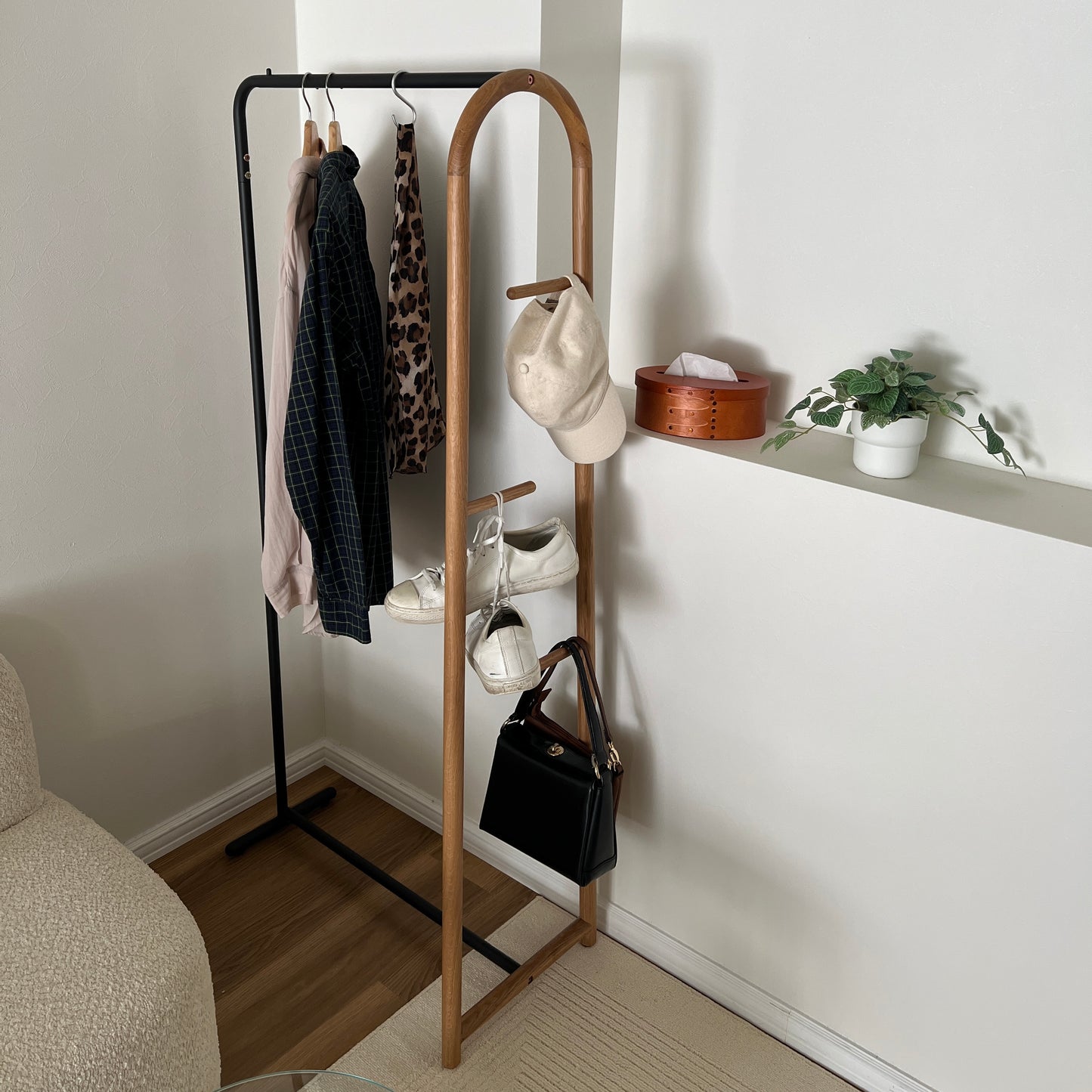 オーク材とブラックスチールのハンガーラックに洋服と帽子、スニーカー、バッグをかけている様子
