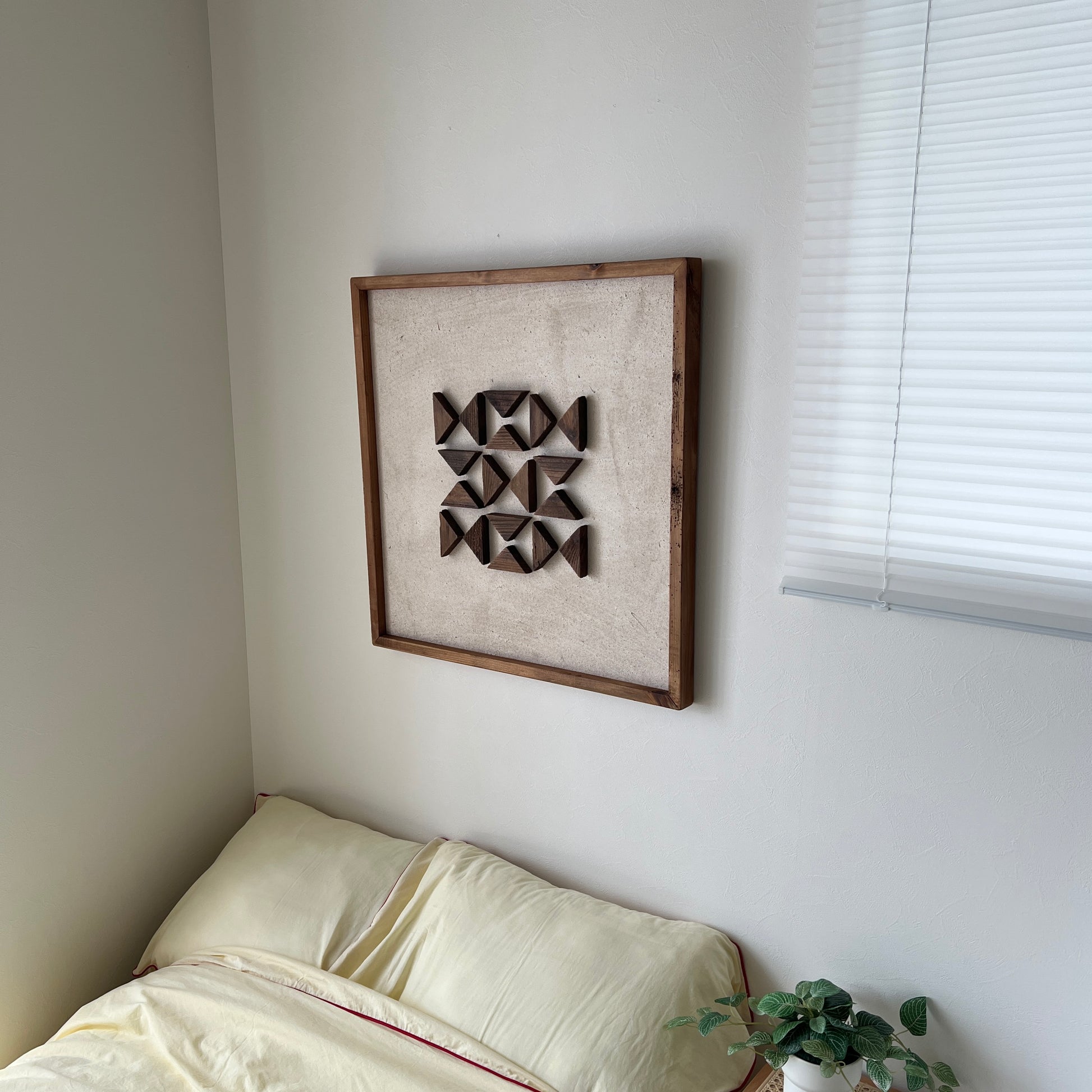 三角形の立体的なウッドパーツが幾何学的に貼り付けられたアートがベッドサイドの壁にかかっている様子
