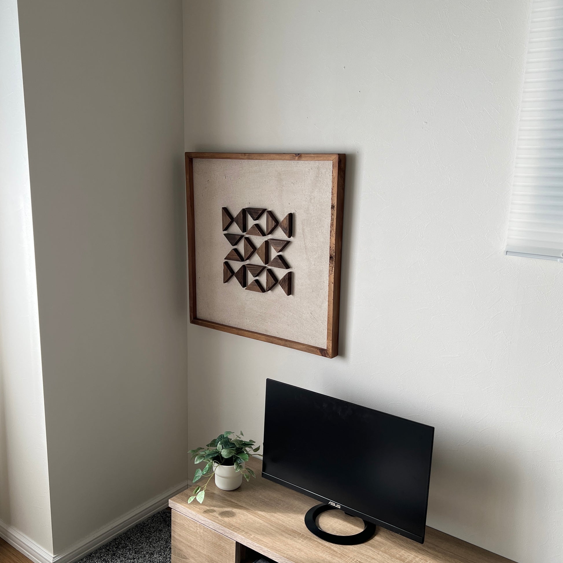 三角形の立体的なウッドパーツが幾何学的に貼り付けられたアートが部屋の隅の壁にかかっている様子