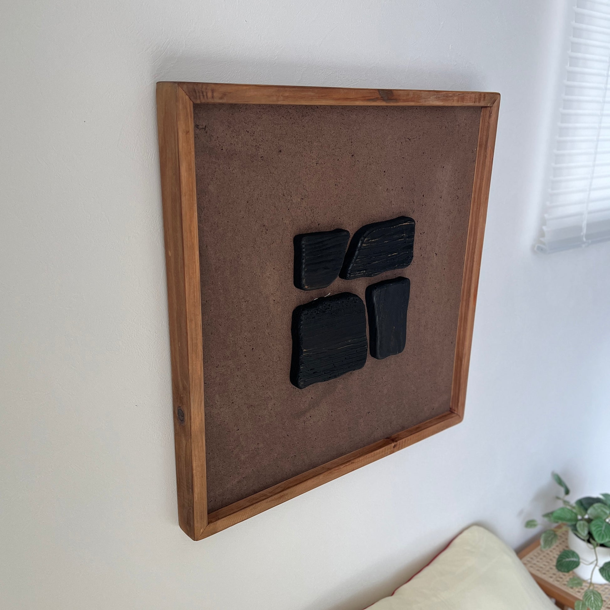 ブラックのウッドピースが立体的に貼り付けられたアートが壁にかかっている様子