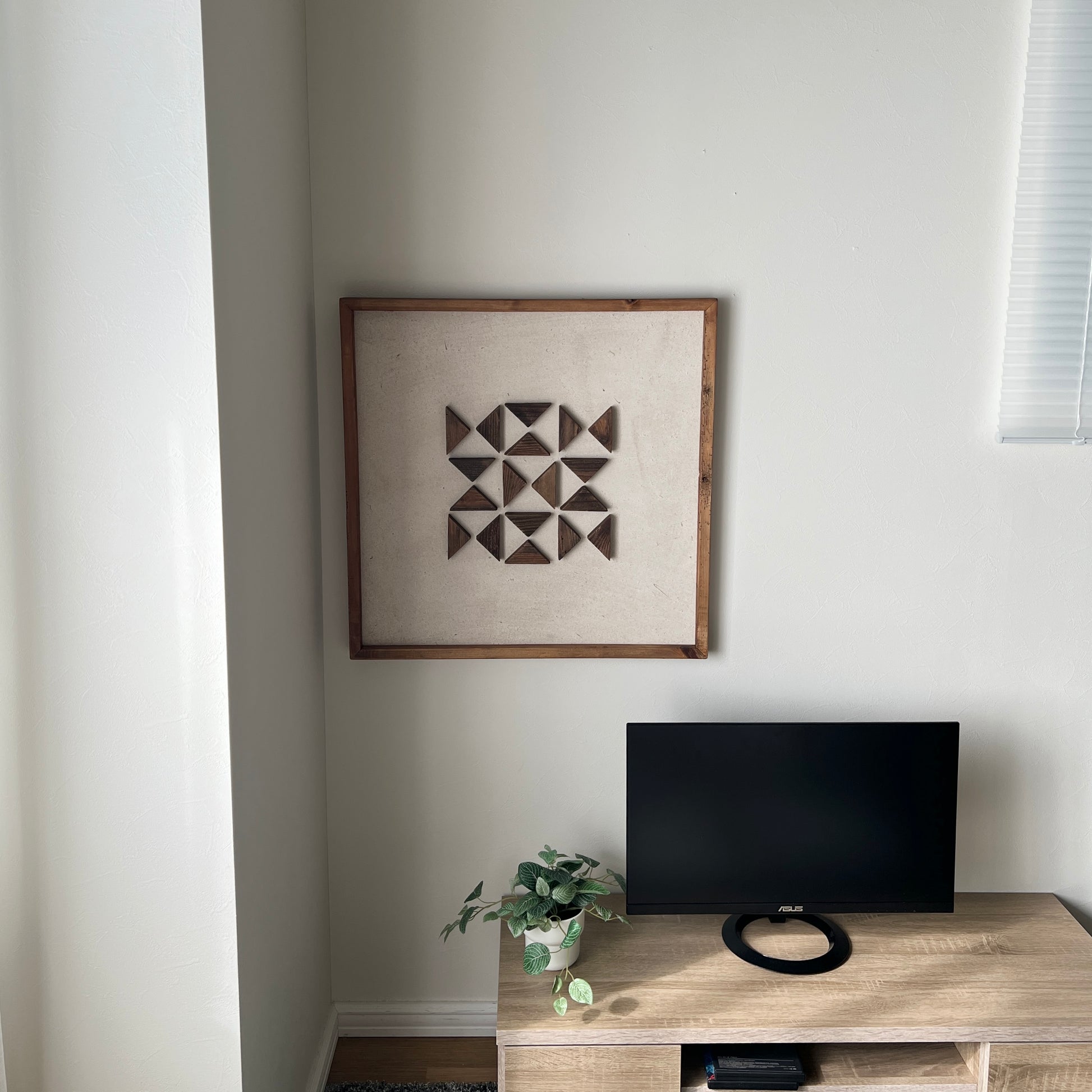 三角形の立体的なウッドパーツが幾何学的に貼り付けられたアートが部屋の隅の壁にかかっている様子