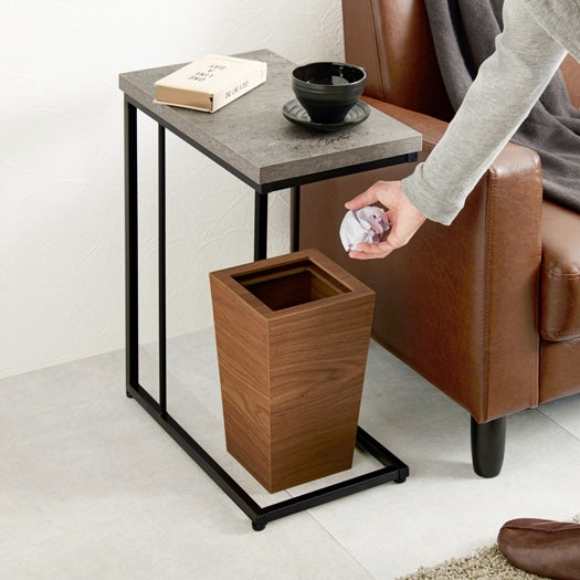 リビングでブラウンの革製ソファの隣に置いてあるコンクリ風デザインのサイドテーブルの下にゴミ箱が設置されている部屋の様子