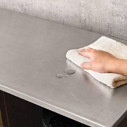 ダークブラウンのステンレス天板コンセント付きキッチンカウンターに溢れた水を拭き取ろうとしている様子