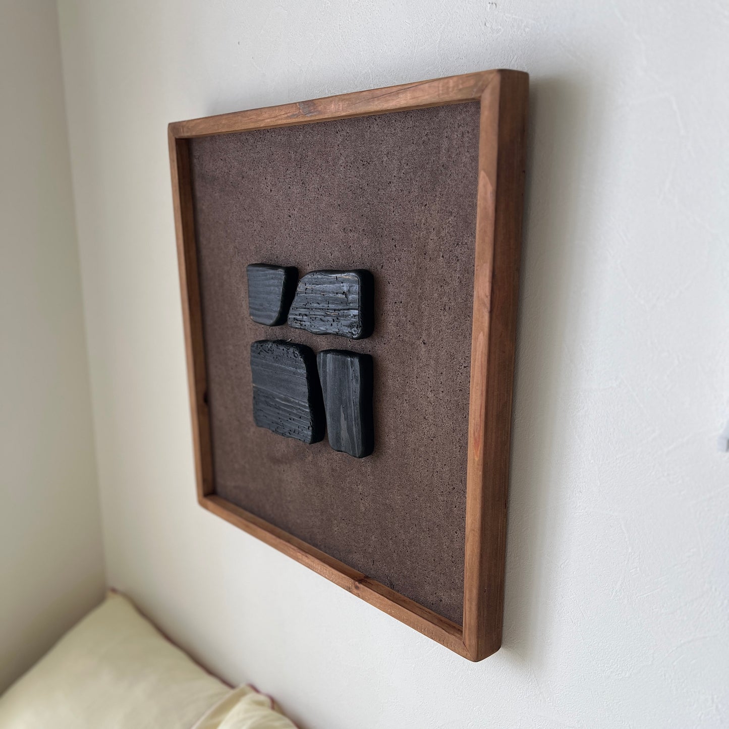 ブラックのウッドピースが立体的に貼り付けられたアートが壁にかかっている様子