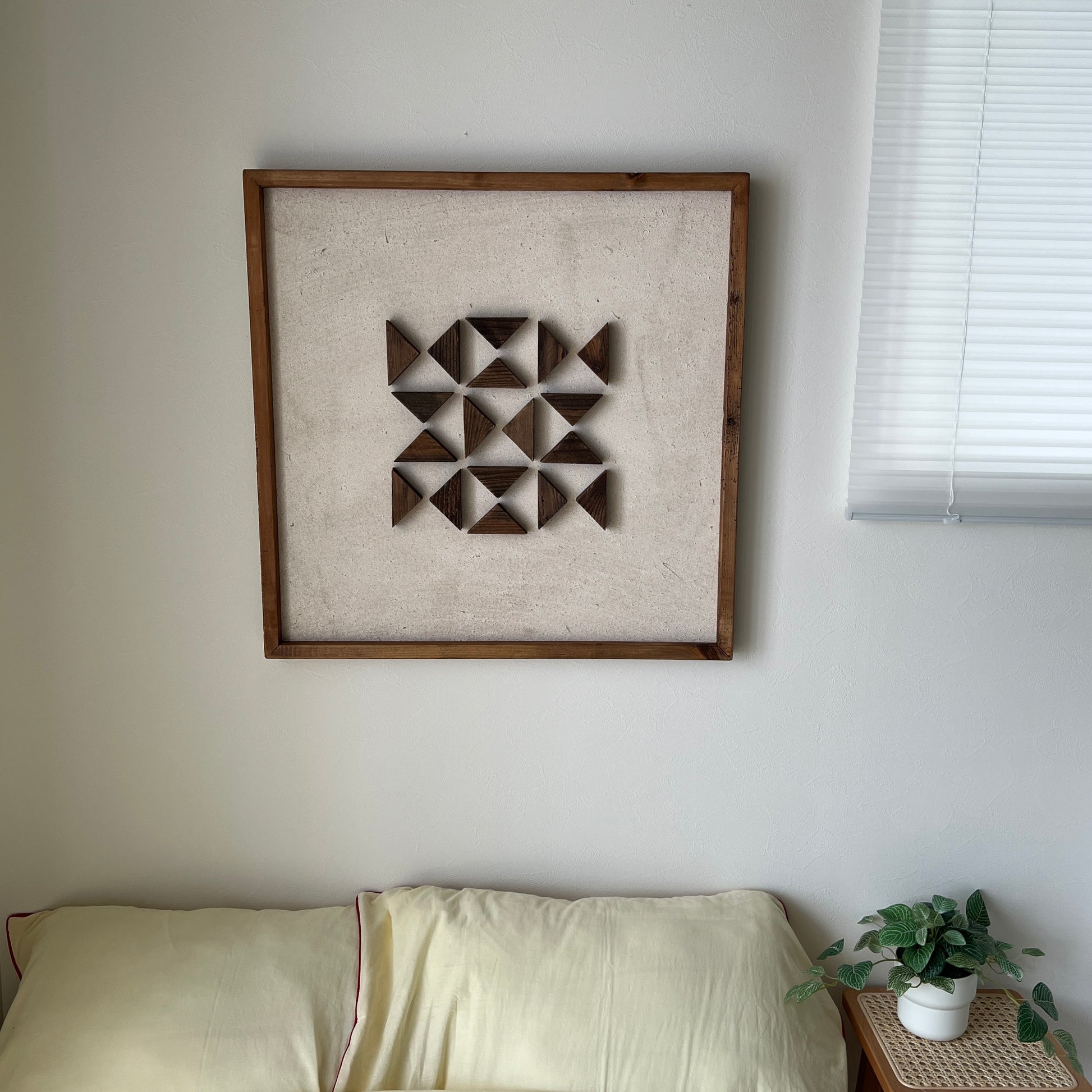 三角形の立体的なウッドパーツが幾何学的に貼り付けられたアートが壁にかかっている様子