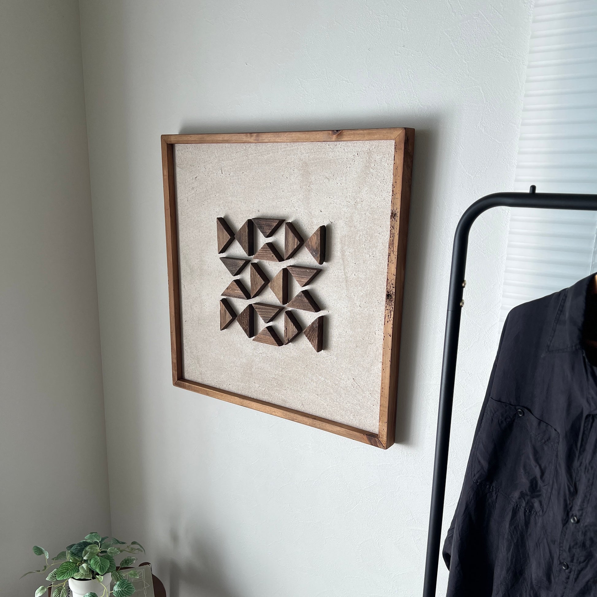 三角形の立体的なウッドパーツを幾何学的に貼り付けたアートが壁にかかっている様子