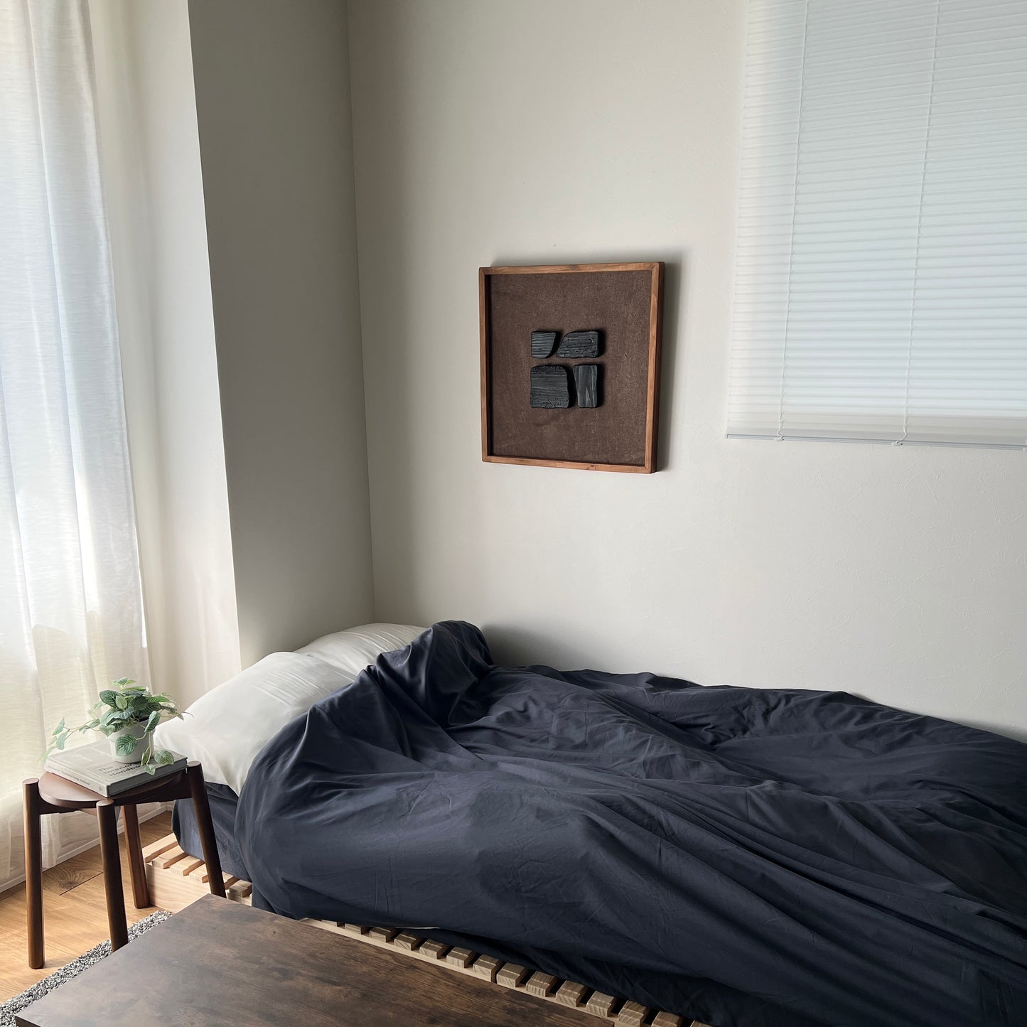 ブラックのウッドピースが立体的に貼り付けられたアートがベッドサイドの壁にかかっている様子