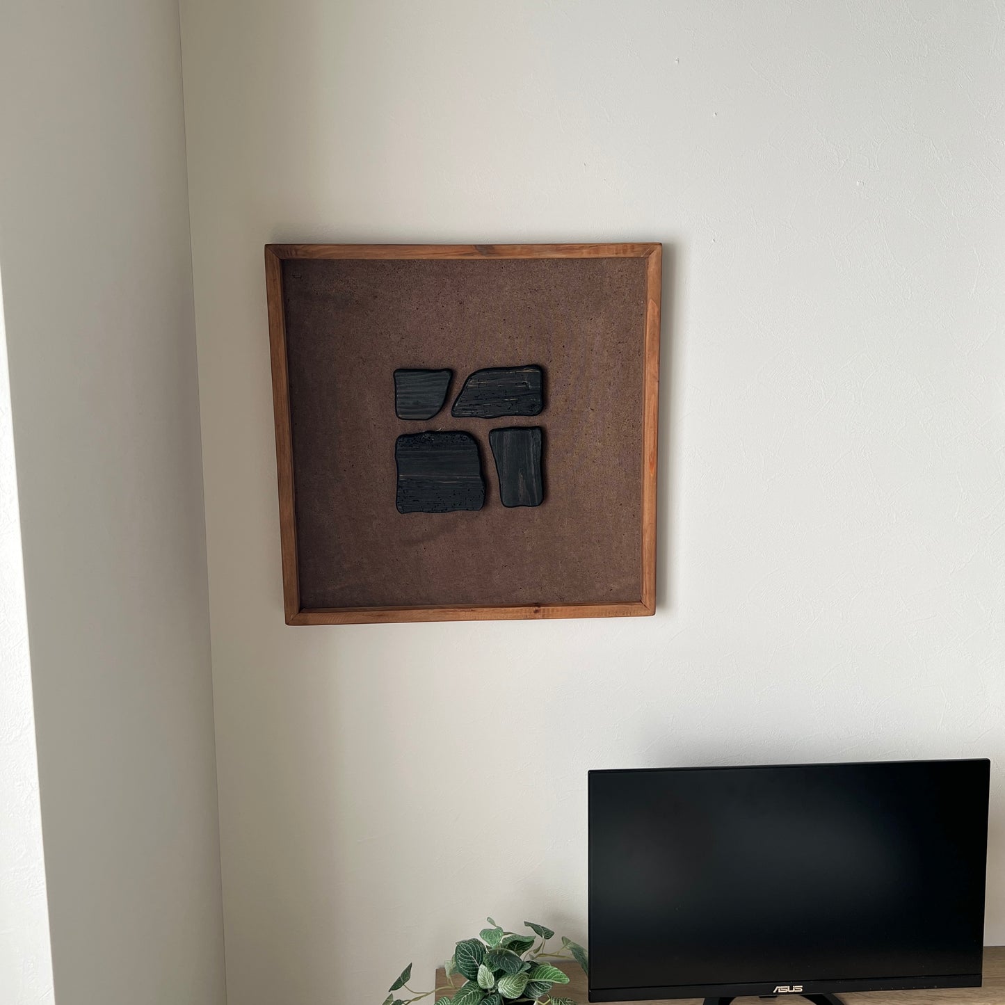ブラックのウッドピースが立体的に貼り付けられたアートが壁にかかっている様子
