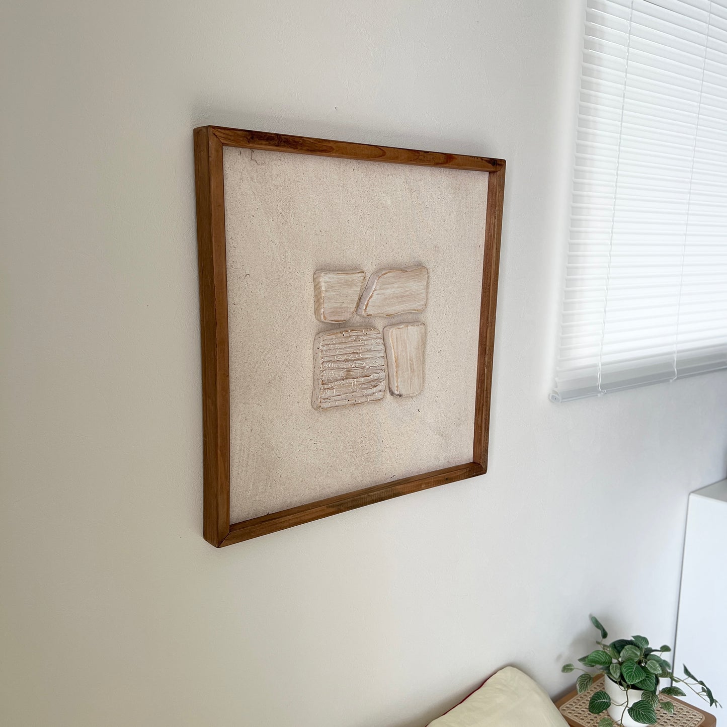 ベージュの立体的なウッドピースが貼り付けられたアートが壁にかかっている様子