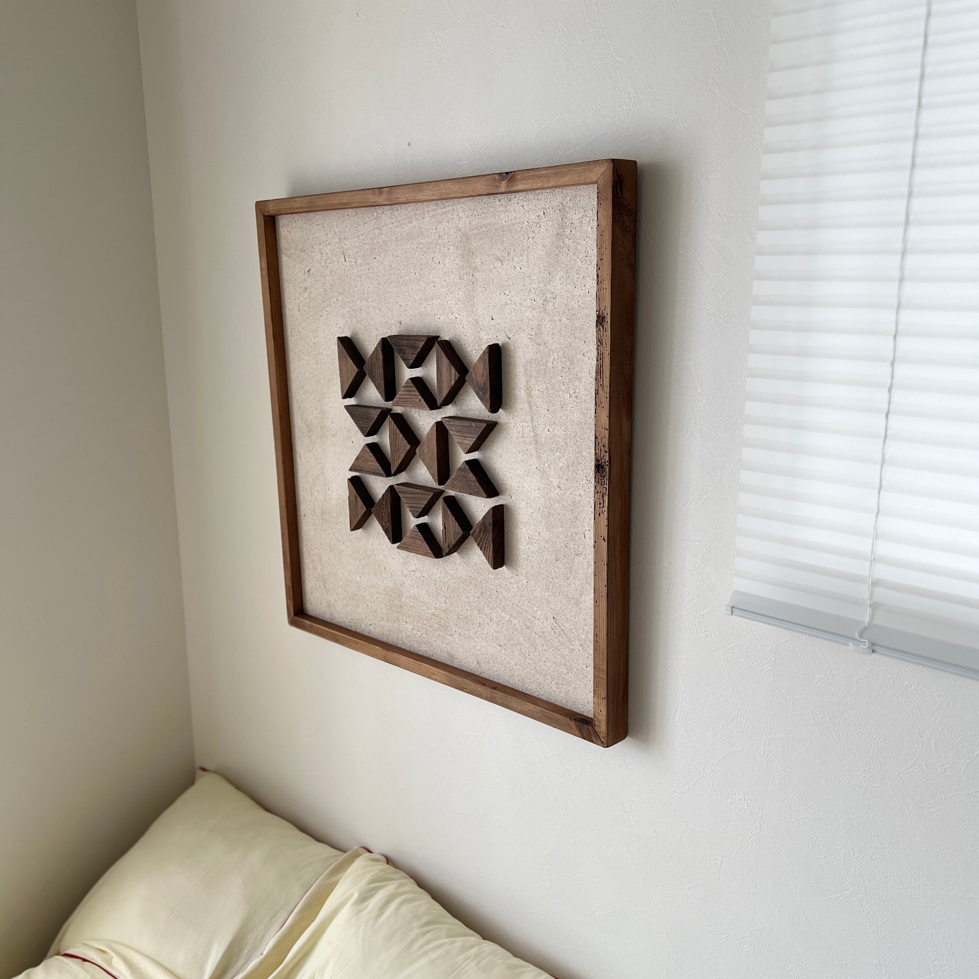 三角形の立体的なウッドパーツが幾何学的に貼り付けられたアートが壁にかかっている様子