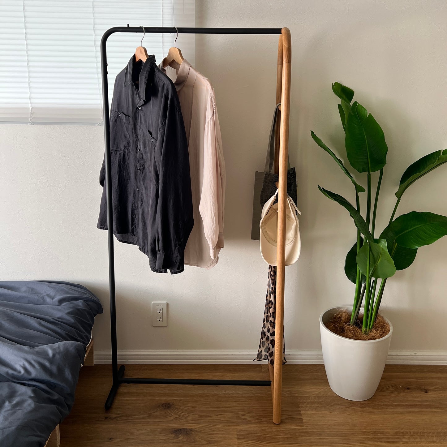 オーク材とブラックスチールのハンガーラックをベッド横に置いている様子