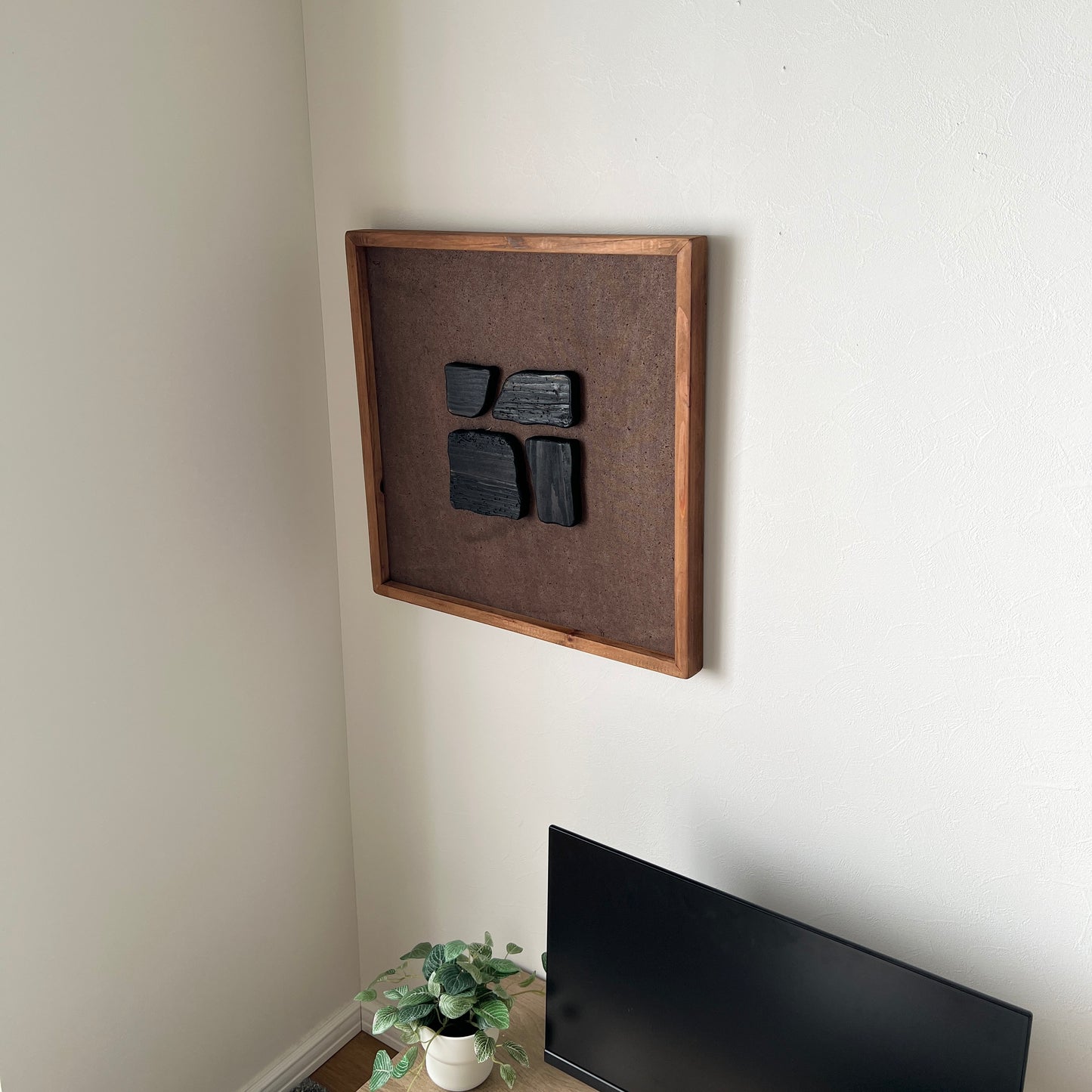 ブラックのウッドピースが立体的に貼り付けられたアートが壁にかかっている様子