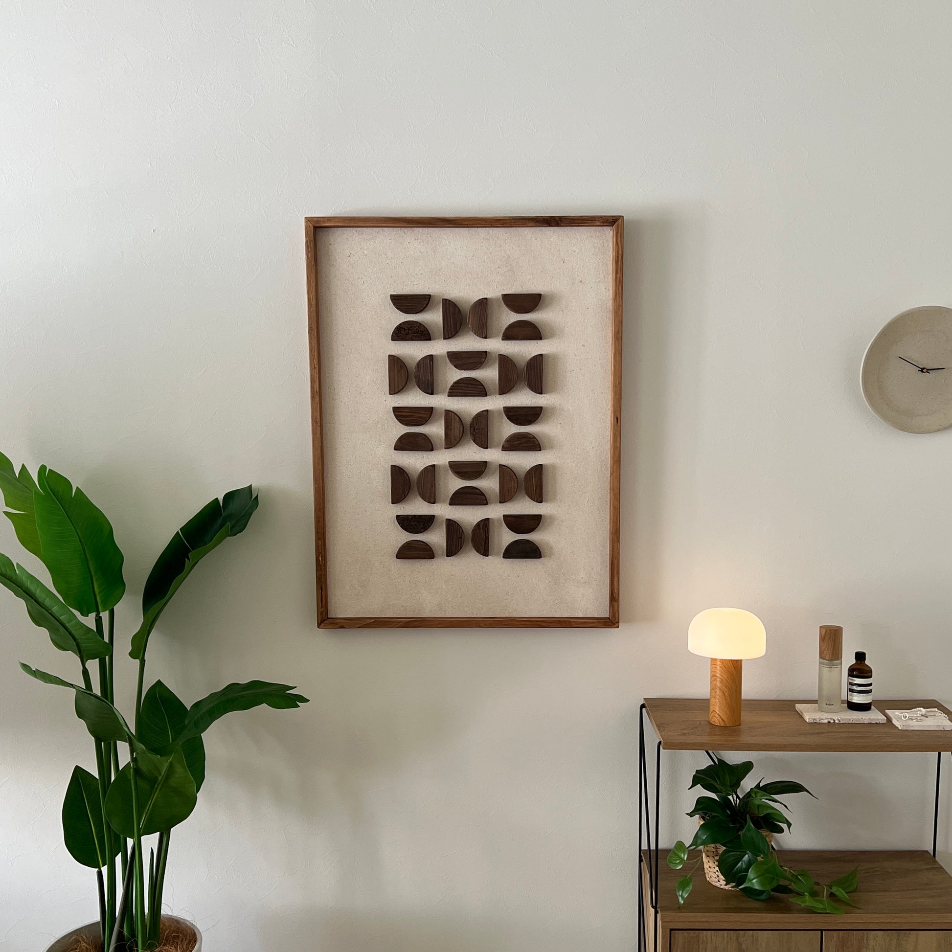 半円型の立体的なウッドパーツが幾何学的に貼り付けられたアートが部屋の壁にかかっている様子