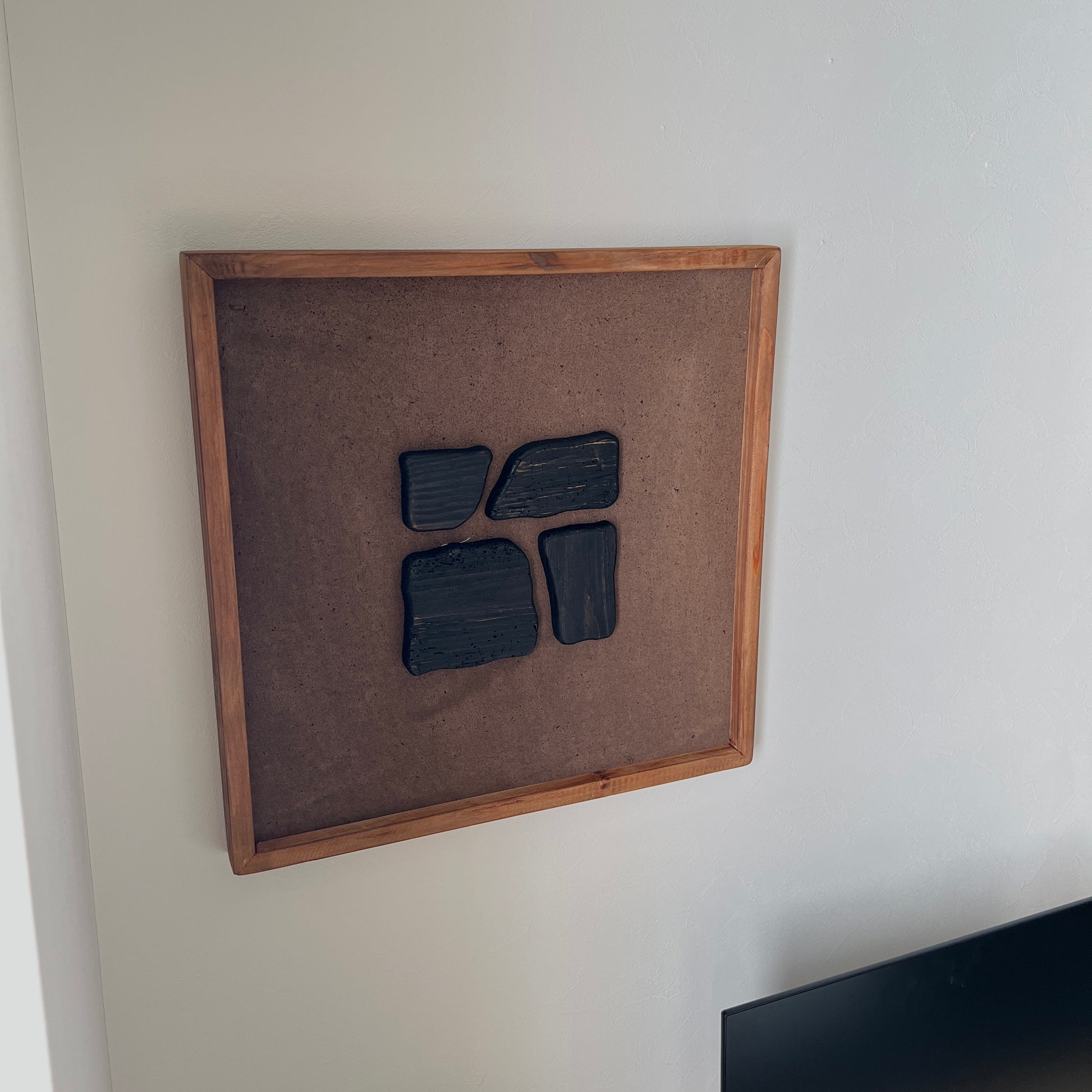 ブラックのウッドピースが立体的に貼り付けられたアートが壁にかかっている様子