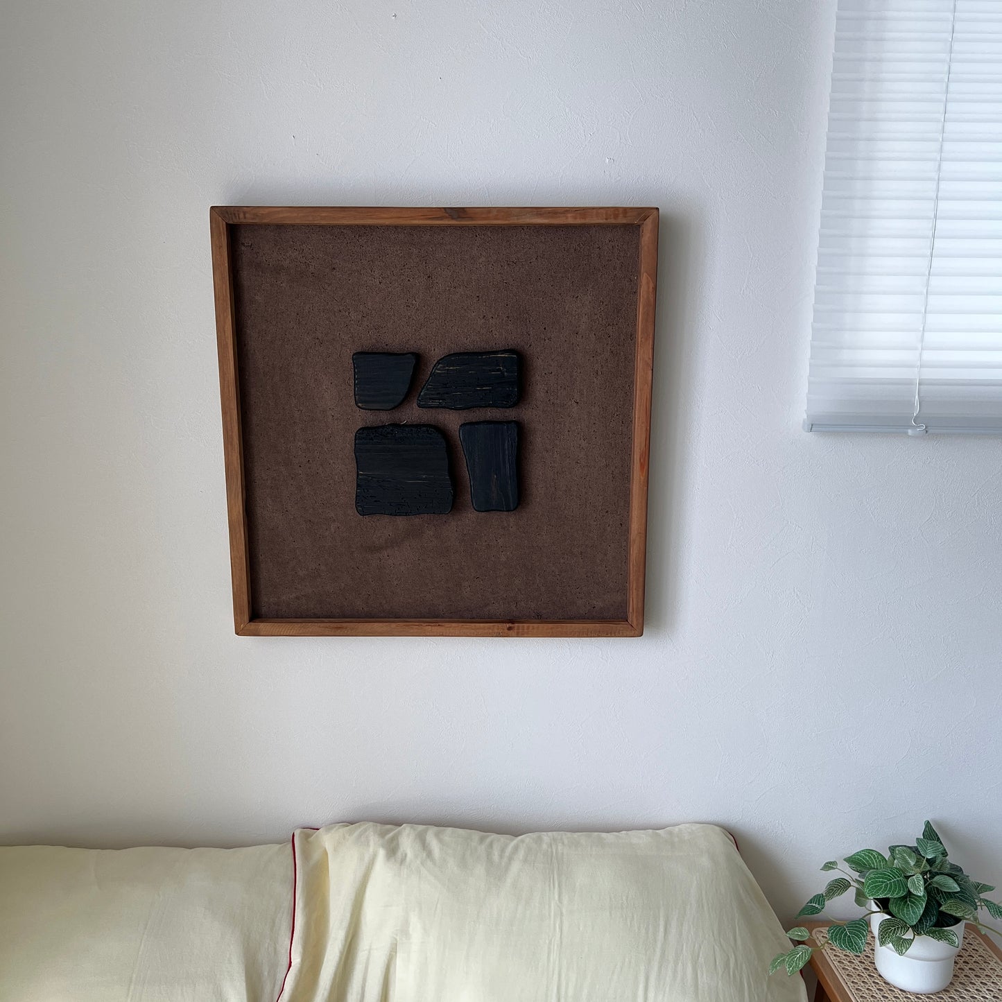 ブラックのウッドピースが立体的に貼り付けられたアートが壁にかかっている様子