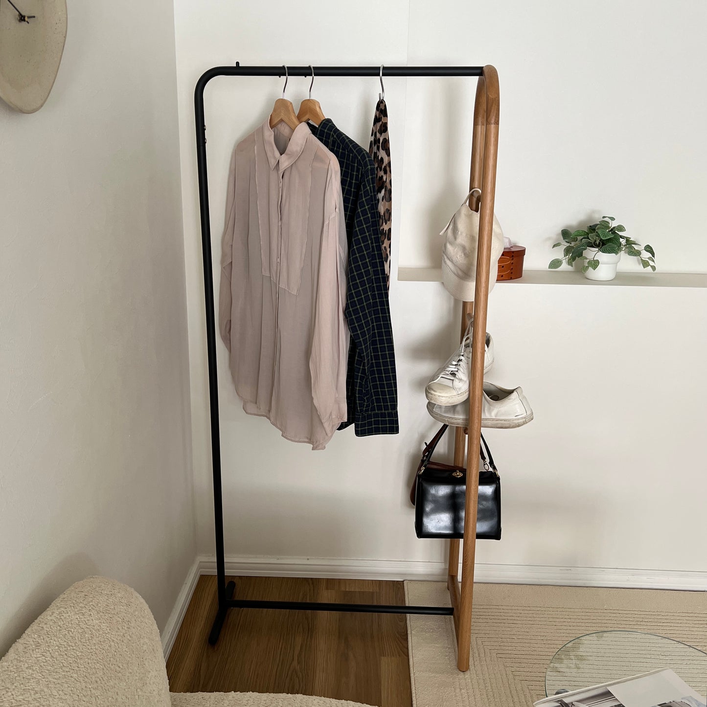 オーク材とブラックスチールのハンガーラックに洋服と帽子、スニーカー、バッグがかかっている様子