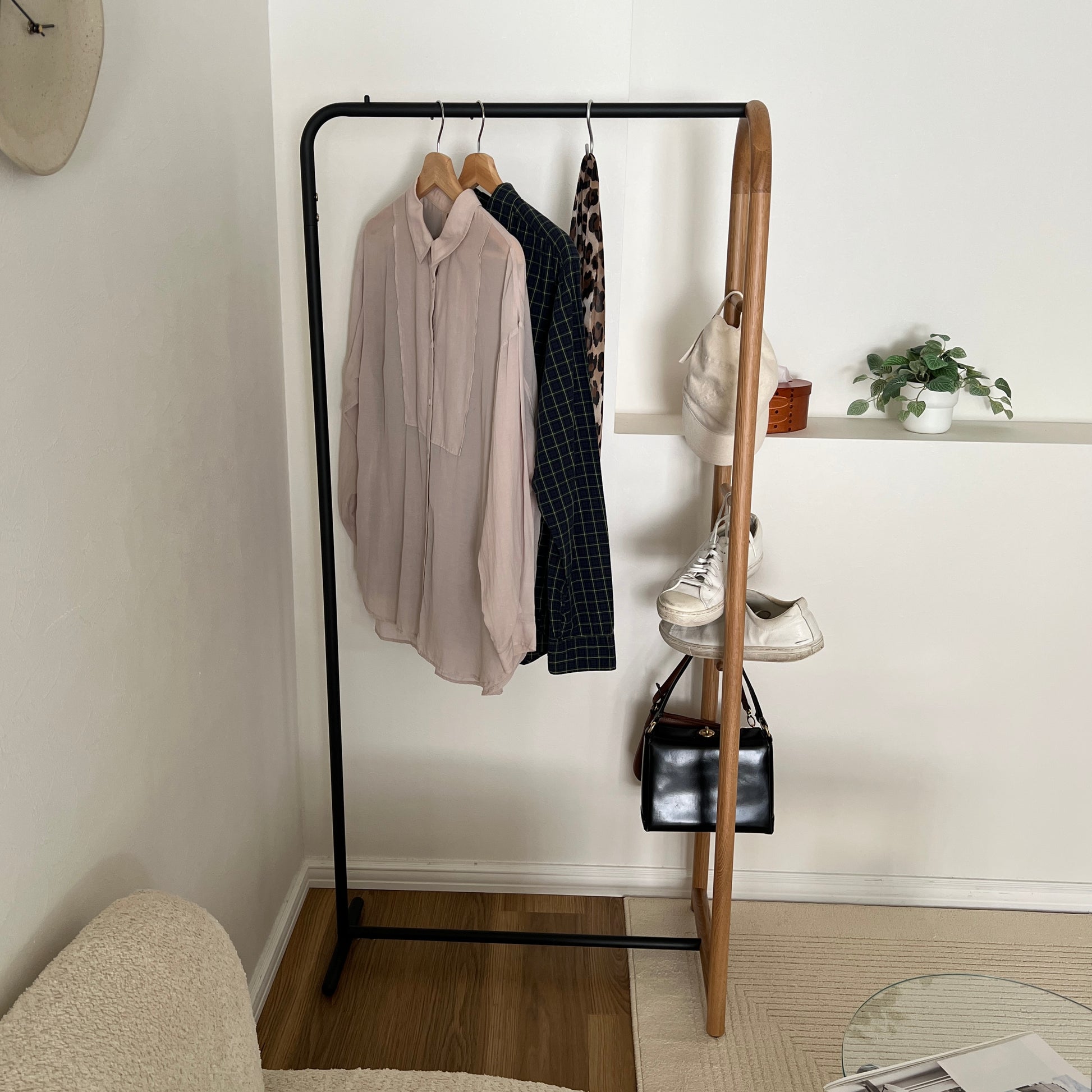 オーク材とブラックスチールのハンガーラックに洋服と帽子、スニーカー、バッグがかかっている様子