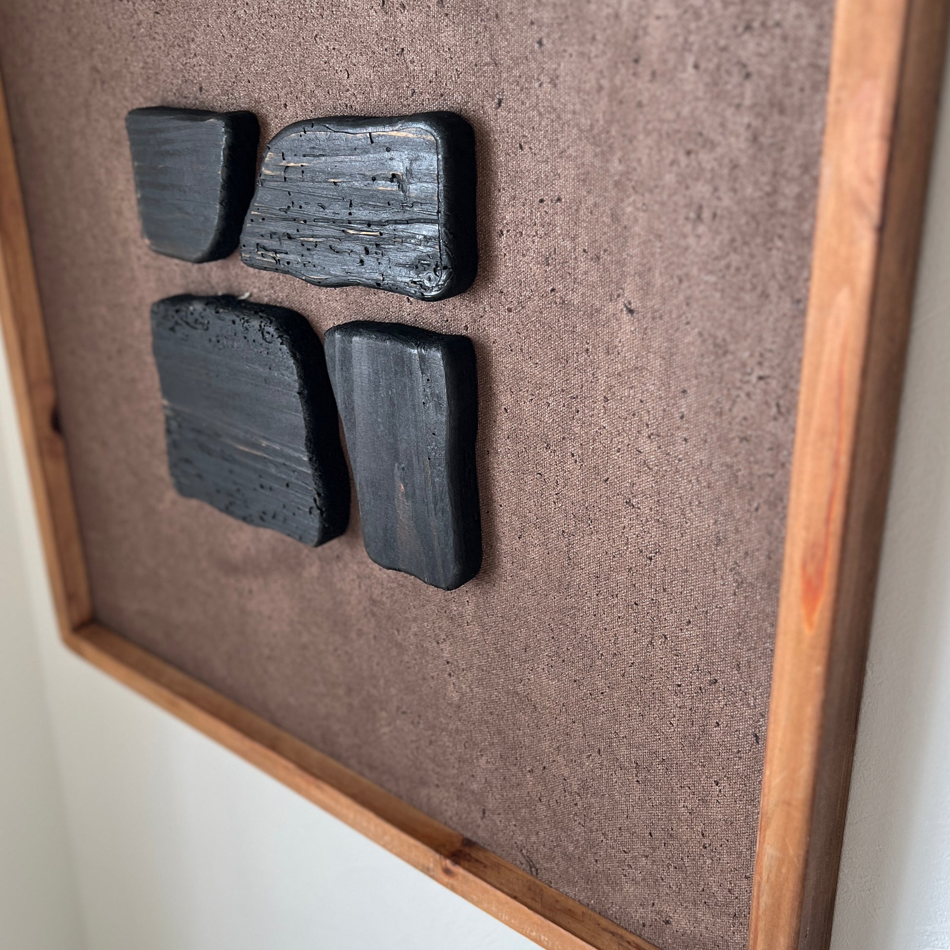 ブラックのウッドピースが立体的に貼り付けられたアートが壁にかかっている様子