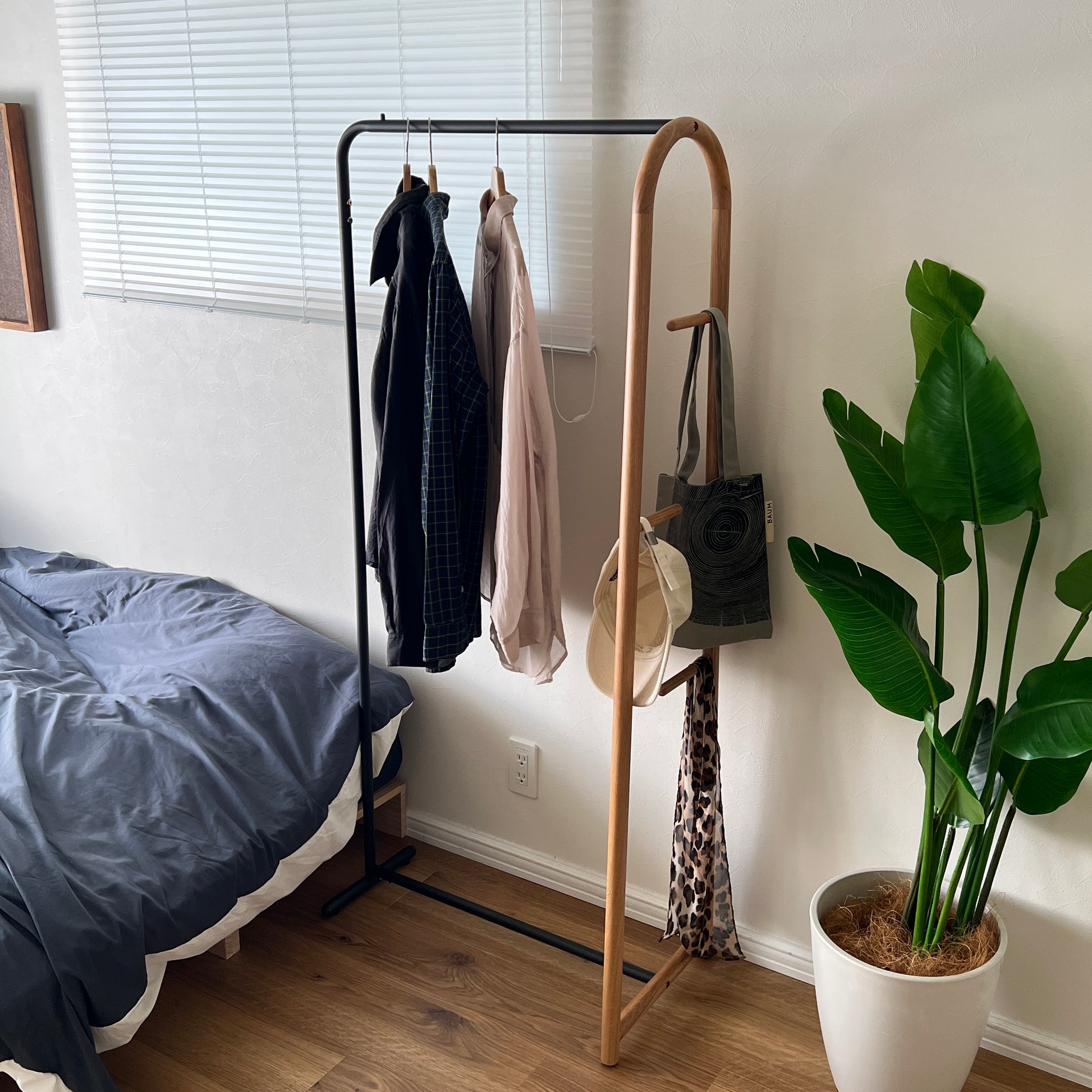 オーク材とブラックスチールのハンガーラックをベッド横に置いている様子