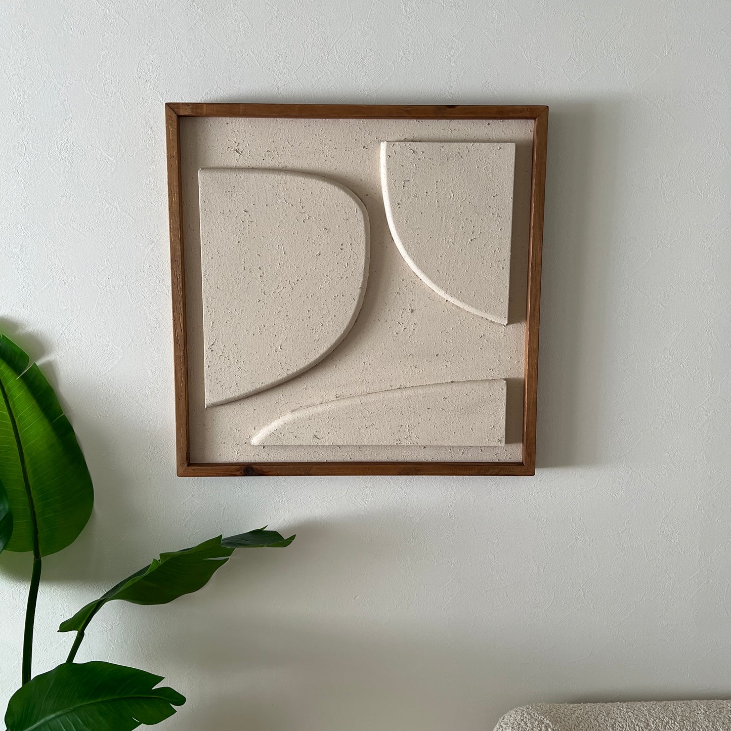 ベージュの立体的なウッドピースが貼り付けられたアートが壁にかけられている