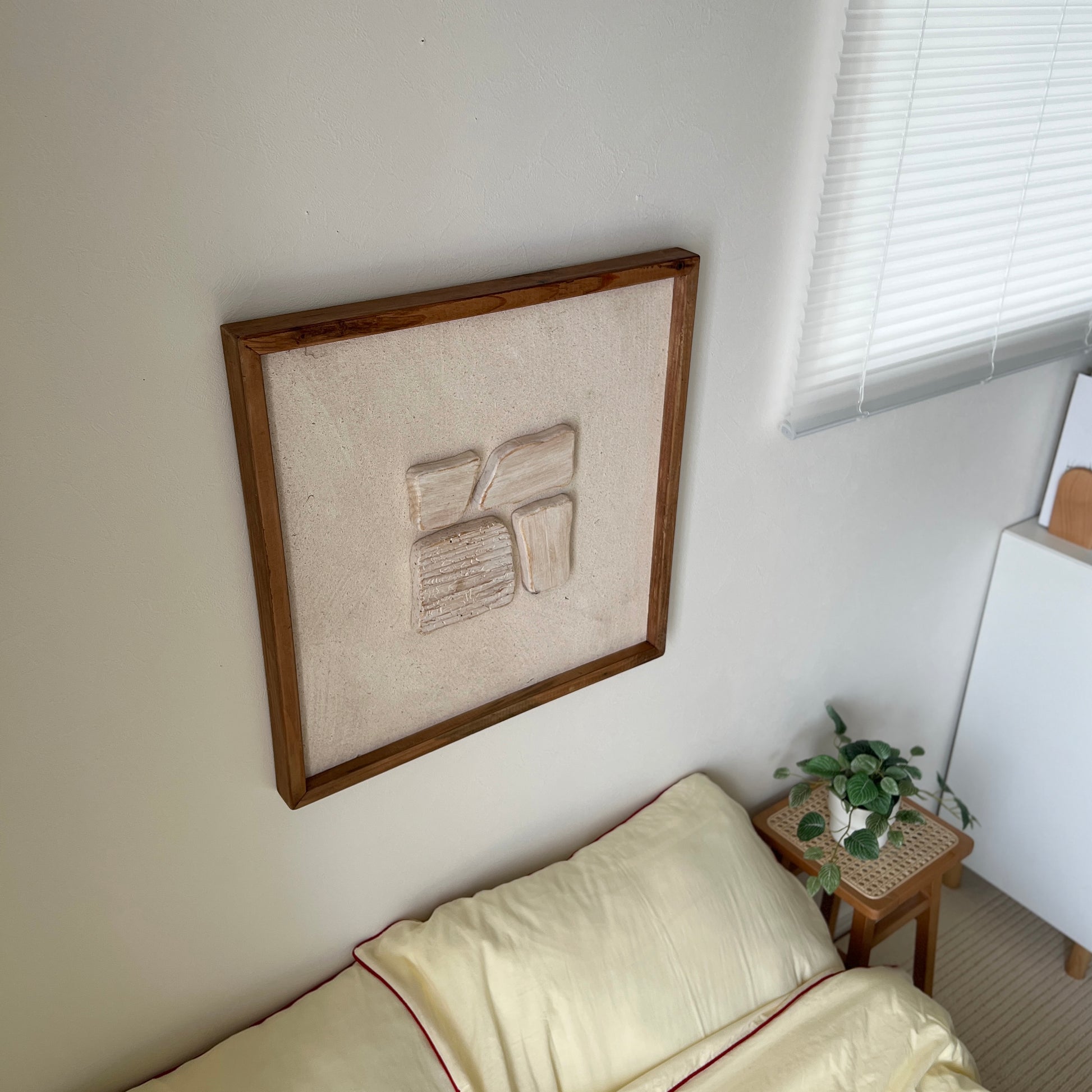 ベージュの立体的なウッドピースが貼り付けられたアートが壁にかかっている様子