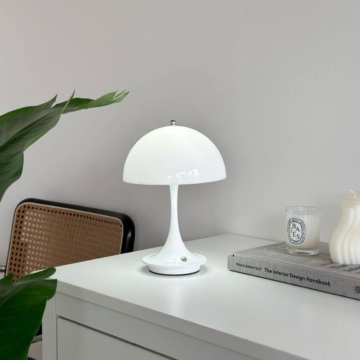 棚の上に置いたホワイトの大きめのシェードにくびれがかった支柱のデザインのランプが点灯している様子