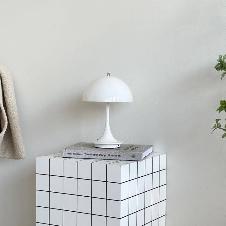 スツールの上に置いたホワイトの大きめのシェードにくびれがかった支柱のデザインのランプ