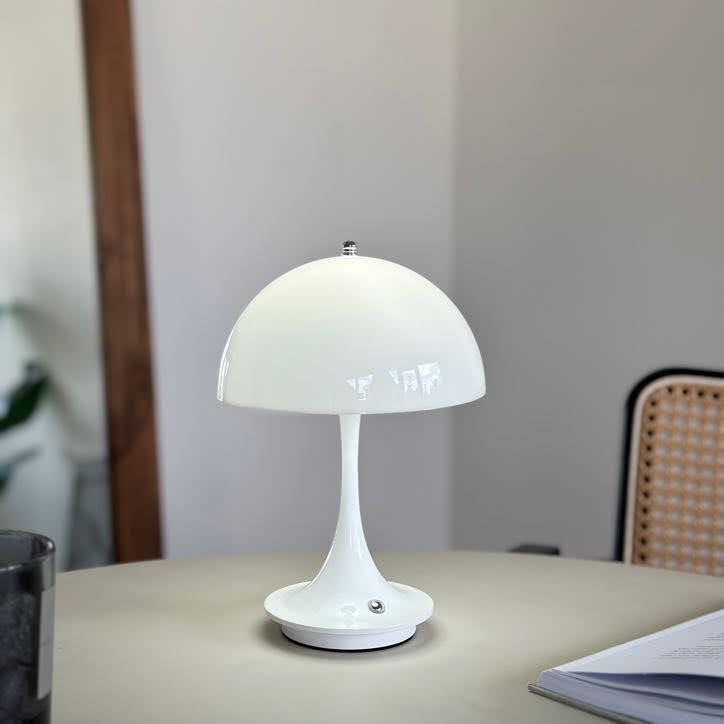 テーブルの上に置いたホワイトの大きめのシェードにくびれがかった支柱のデザインのランプが点灯している様子