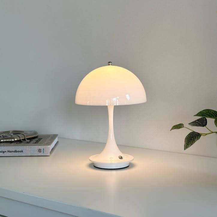 棚の上に置いたホワイトの大きめのシェードにくびれがかった支柱のデザインのランプが点灯している様子