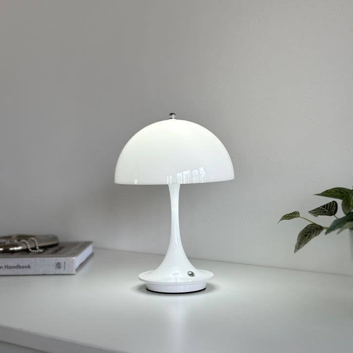 棚の上に置いたホワイトの大きめのシェードにくびれがかった支柱のデザインのランプが点灯している様子