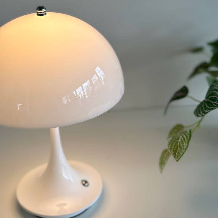 テーブルの上に置いたホワイトの大きめのシェードにくびれがかった支柱のデザインのランプが点灯している様子