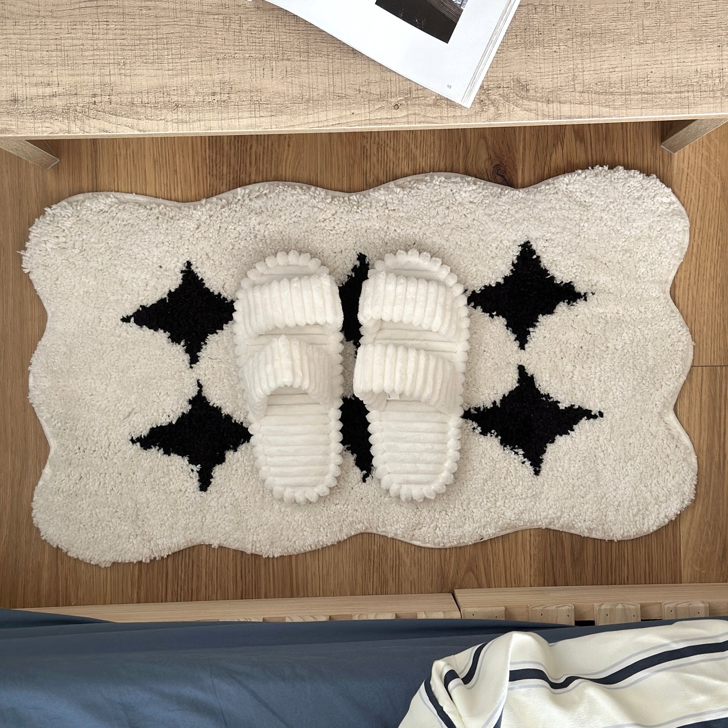 白のもこもこしたデザインでダブルストラップ付きのルームスリッパがベッドサイドに置かれている様子