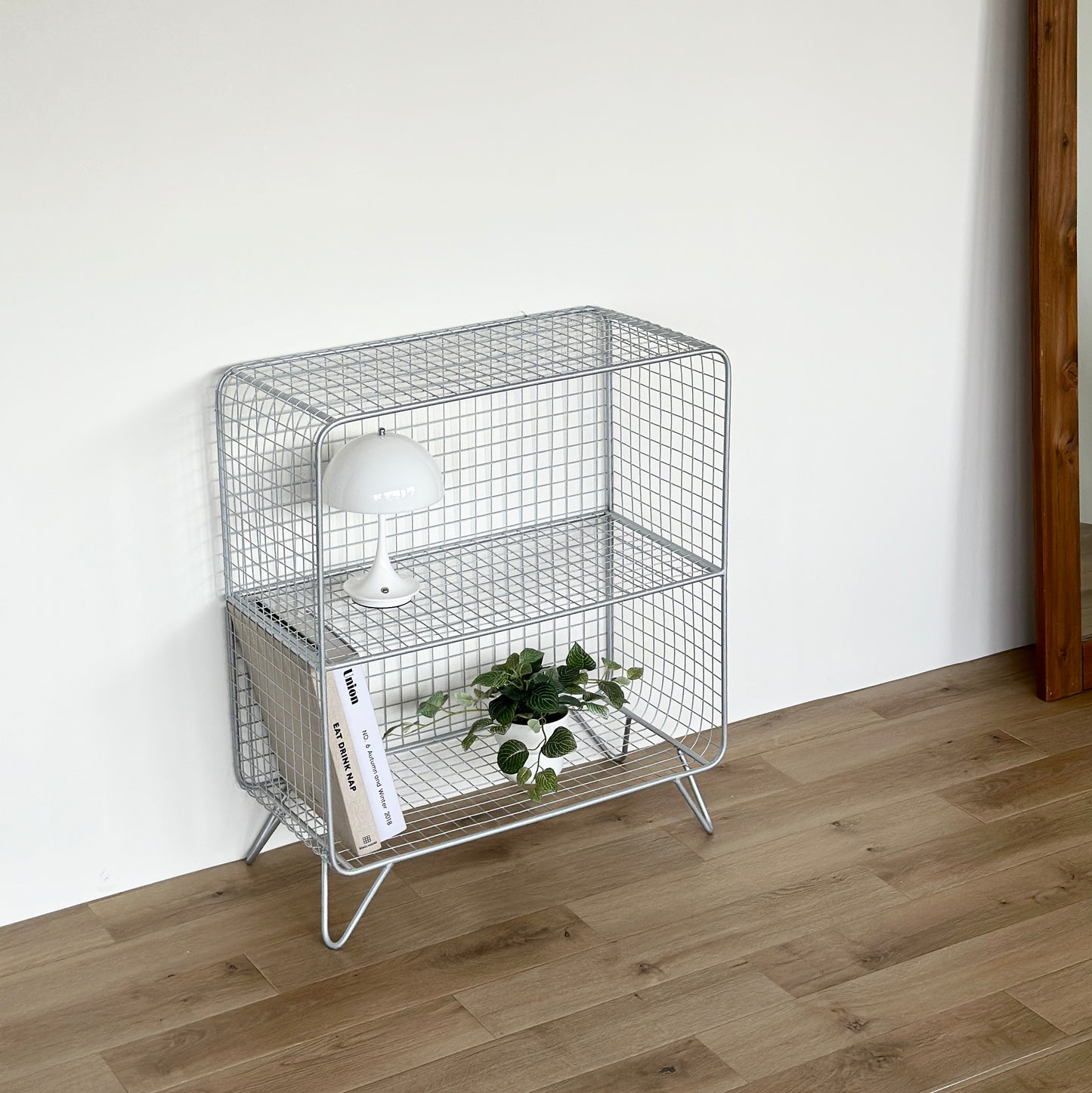 メッシュデザインのシェルフの上段には白のライト、下段には雑誌と植物が置かれてある