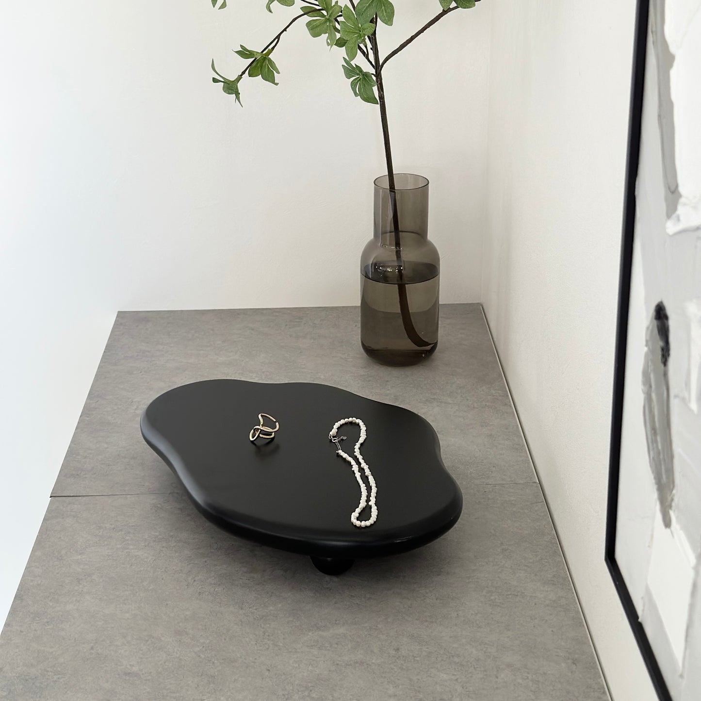 木製の黒の大きなトレイの上にアクセサリーが置かれていて、奥に植物が置かれている