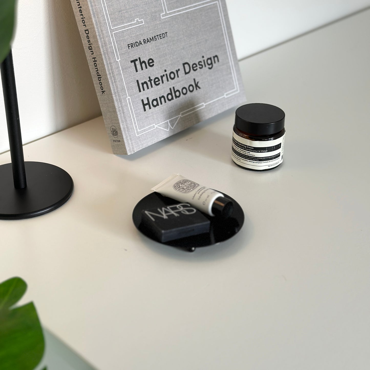 脚付のブラックの鉄製の丸いプレートの上に化粧品が乗っていて、本や植物が周りに置かれている
