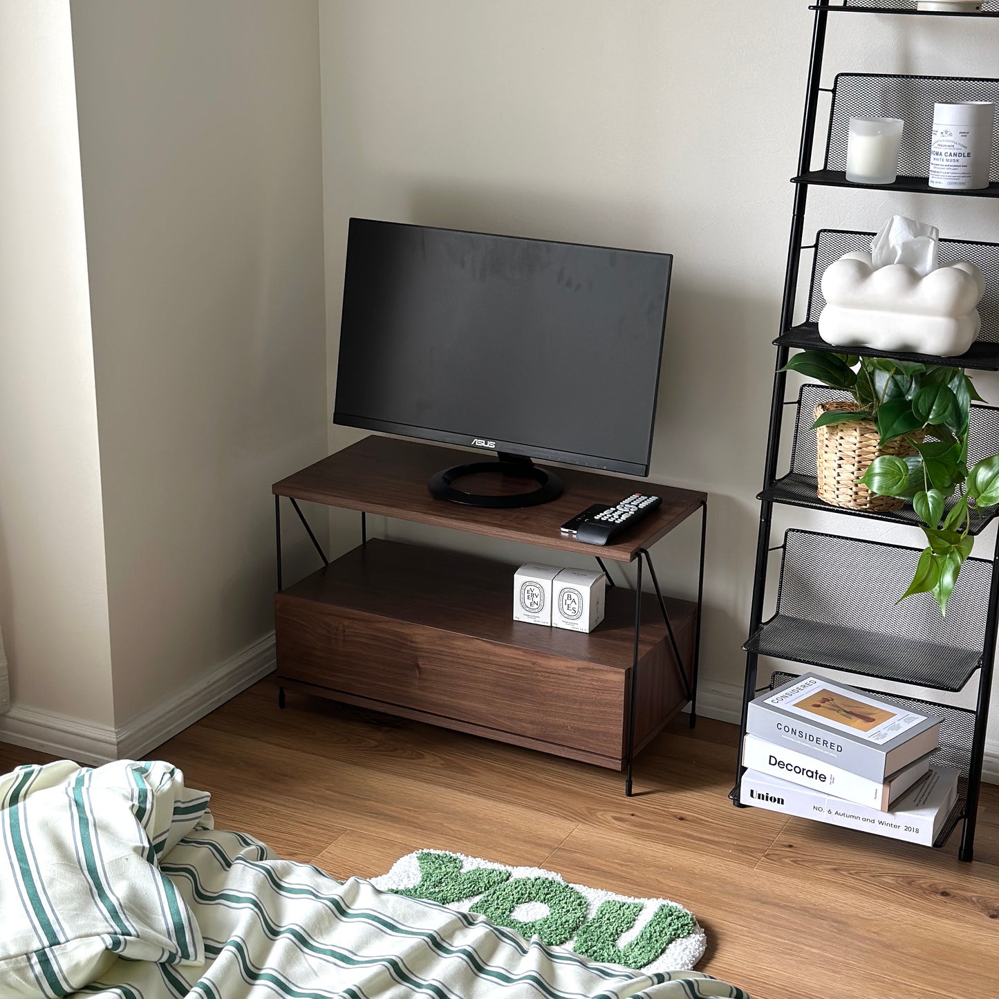 木目のウッドと細いブラックフレームのテレビボードを部屋の隅に置いている様子