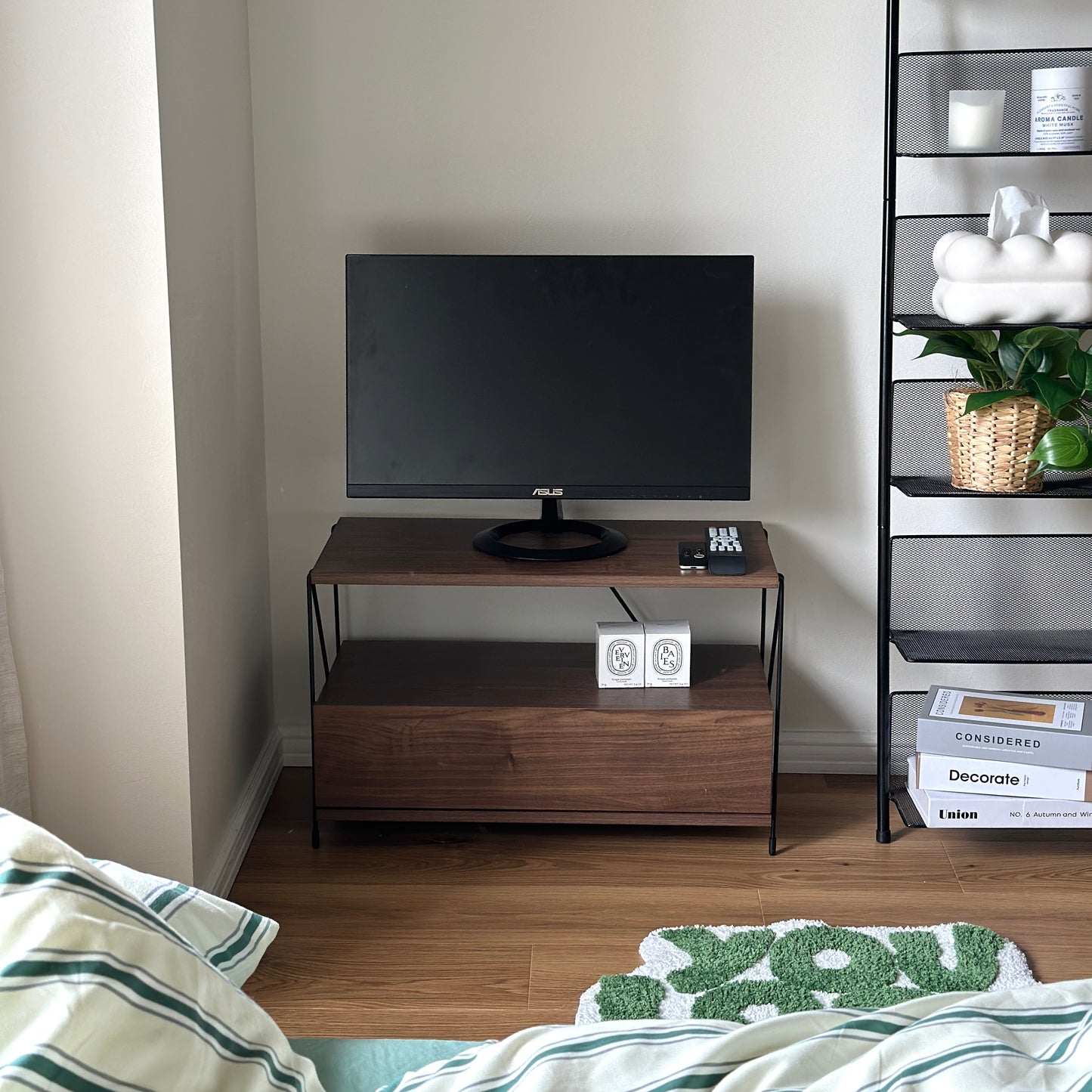 木目のウッドと細いブラックフレームのテレビボードを部屋の隅に置いている様子