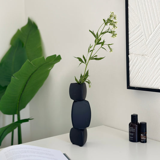 三角柱が重なったデザインのブラックのセラミック製フラワーベースに花が生けてあり、その横に植物がある