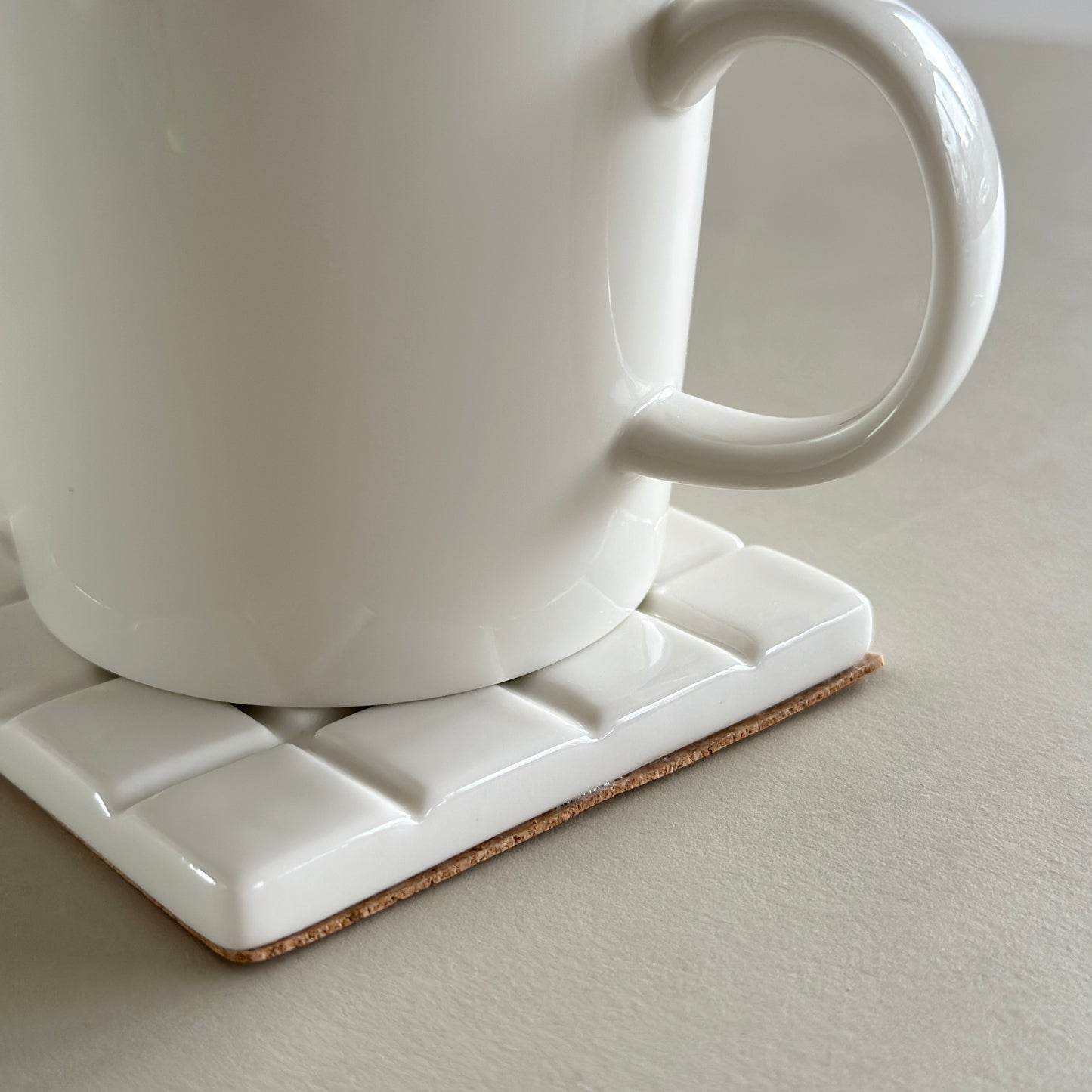 白のタイル柄のコースターの上に白のマグカップが置かれてある