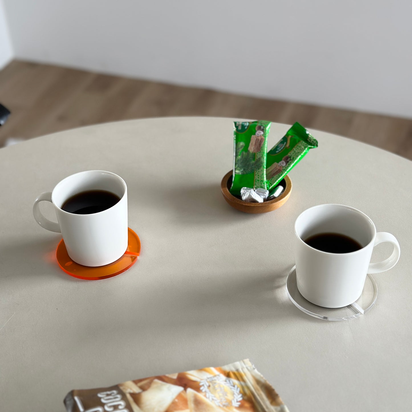 アクリルのクリアとオレンジのコースターにコーヒーが入ったマグカップを置いている様子
