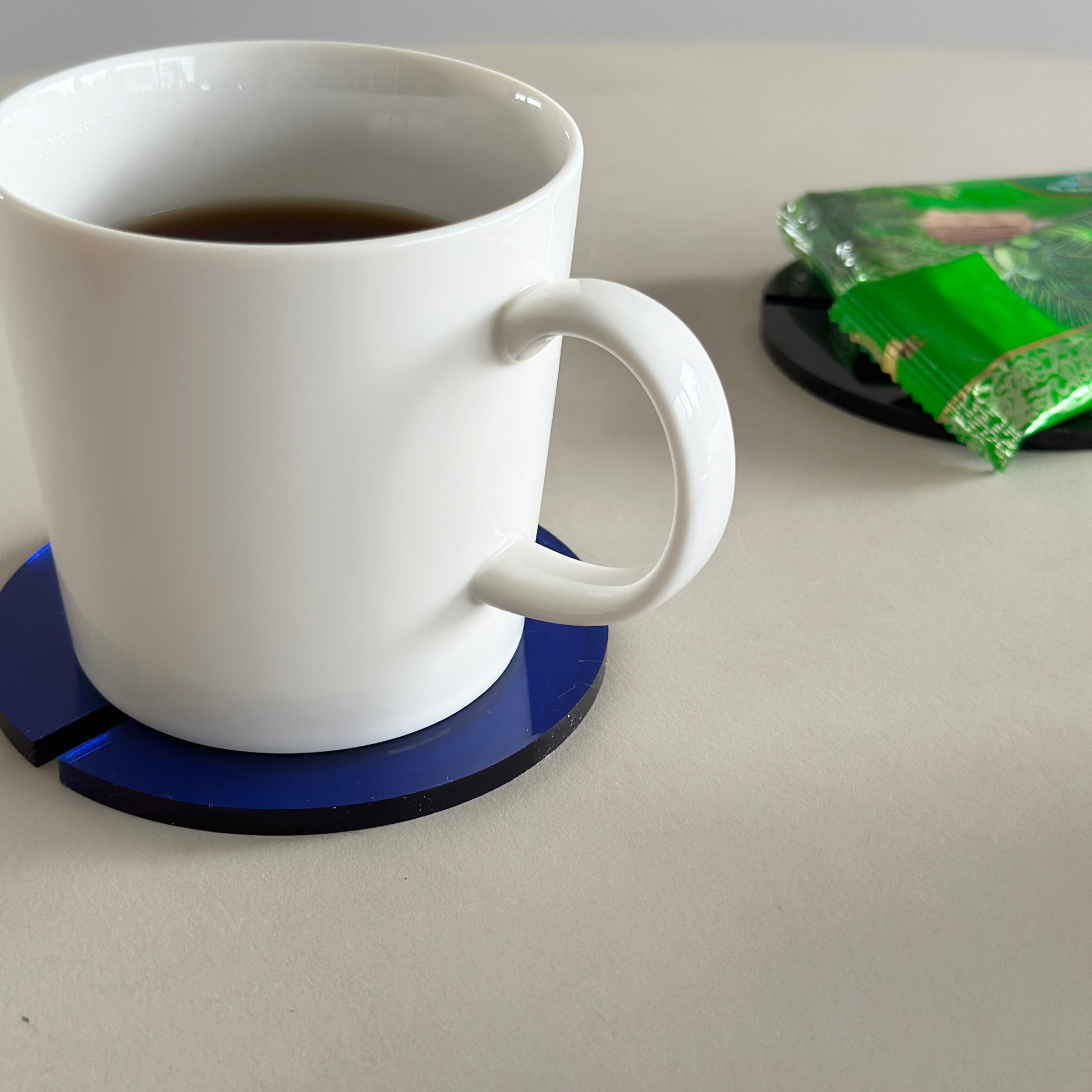 アクリルのブルーのコースターにコーヒーが入ったマグカップを置いている様子