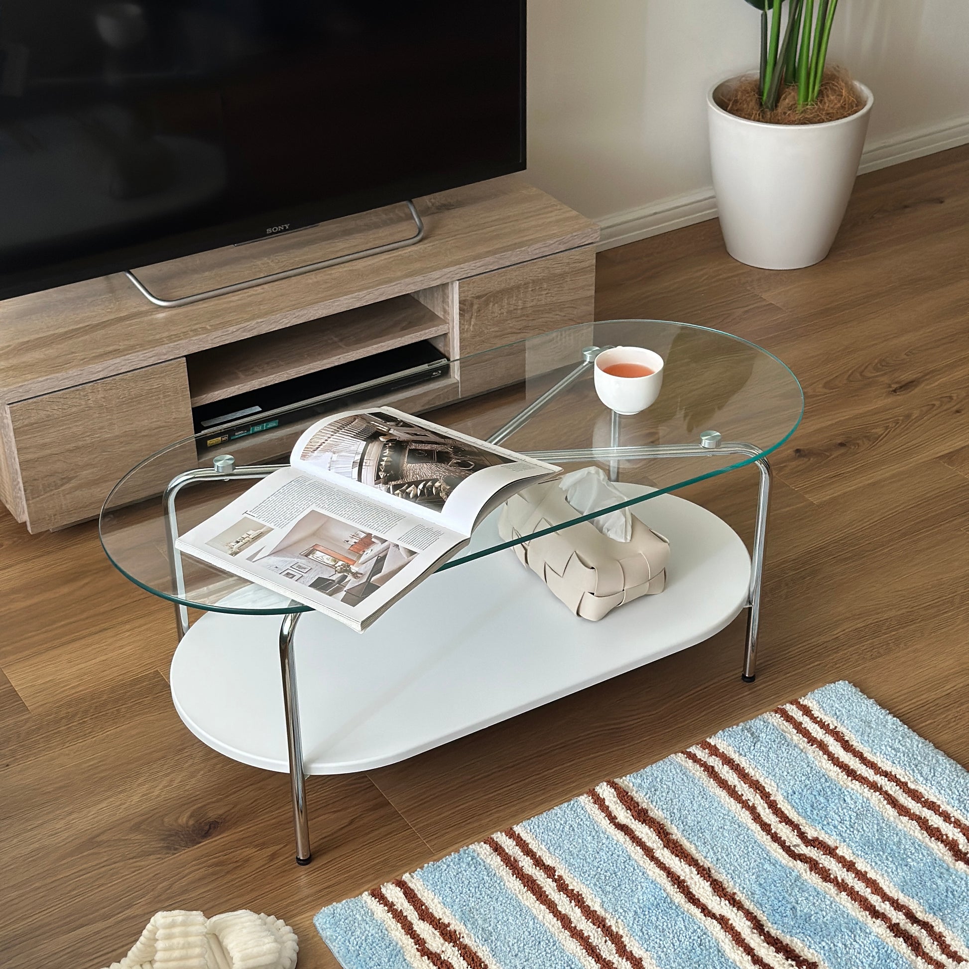 丸みのあるガラス天板のローテーブルの天板上にはコップと雑誌が置かれており、下の棚にはティッシュケースが置かれてある