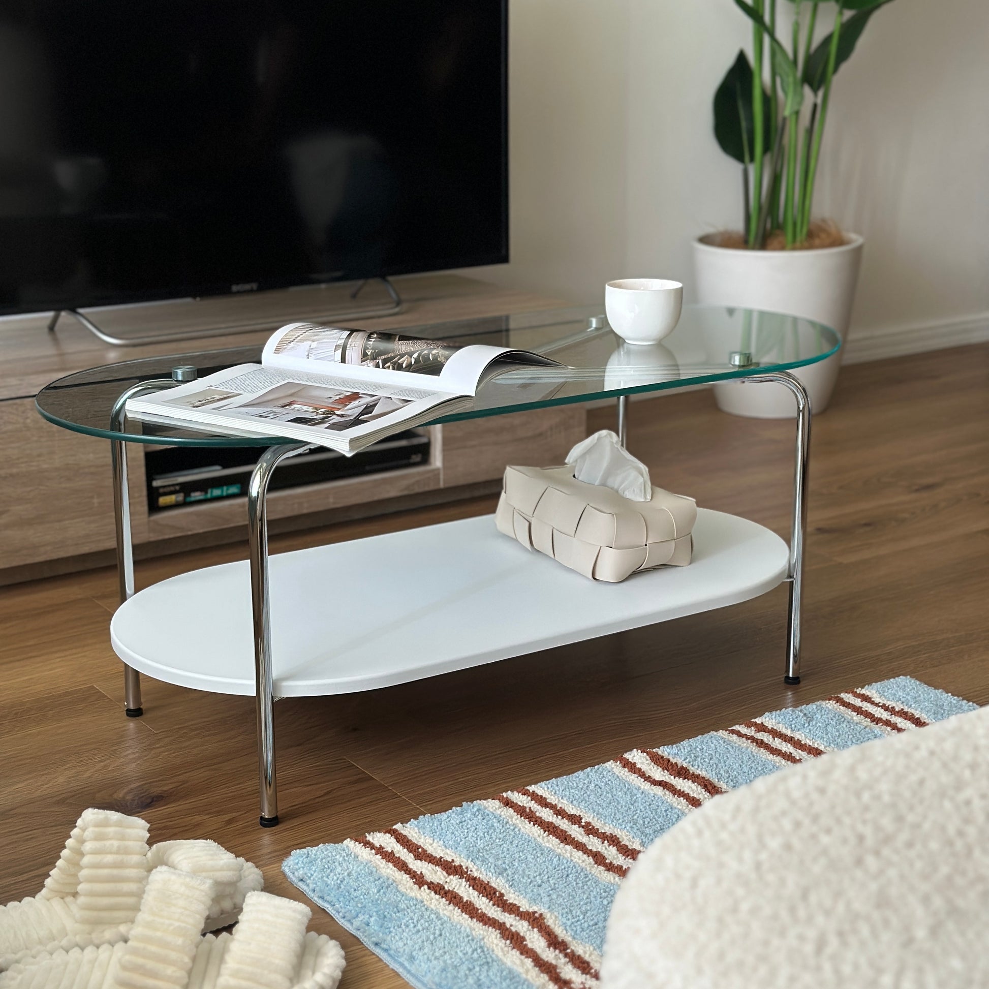 丸みのあるガラス天板のローテーブルの天板上にはコップと雑誌が置かれており、下の棚にはティッシュケースが置かれてある
