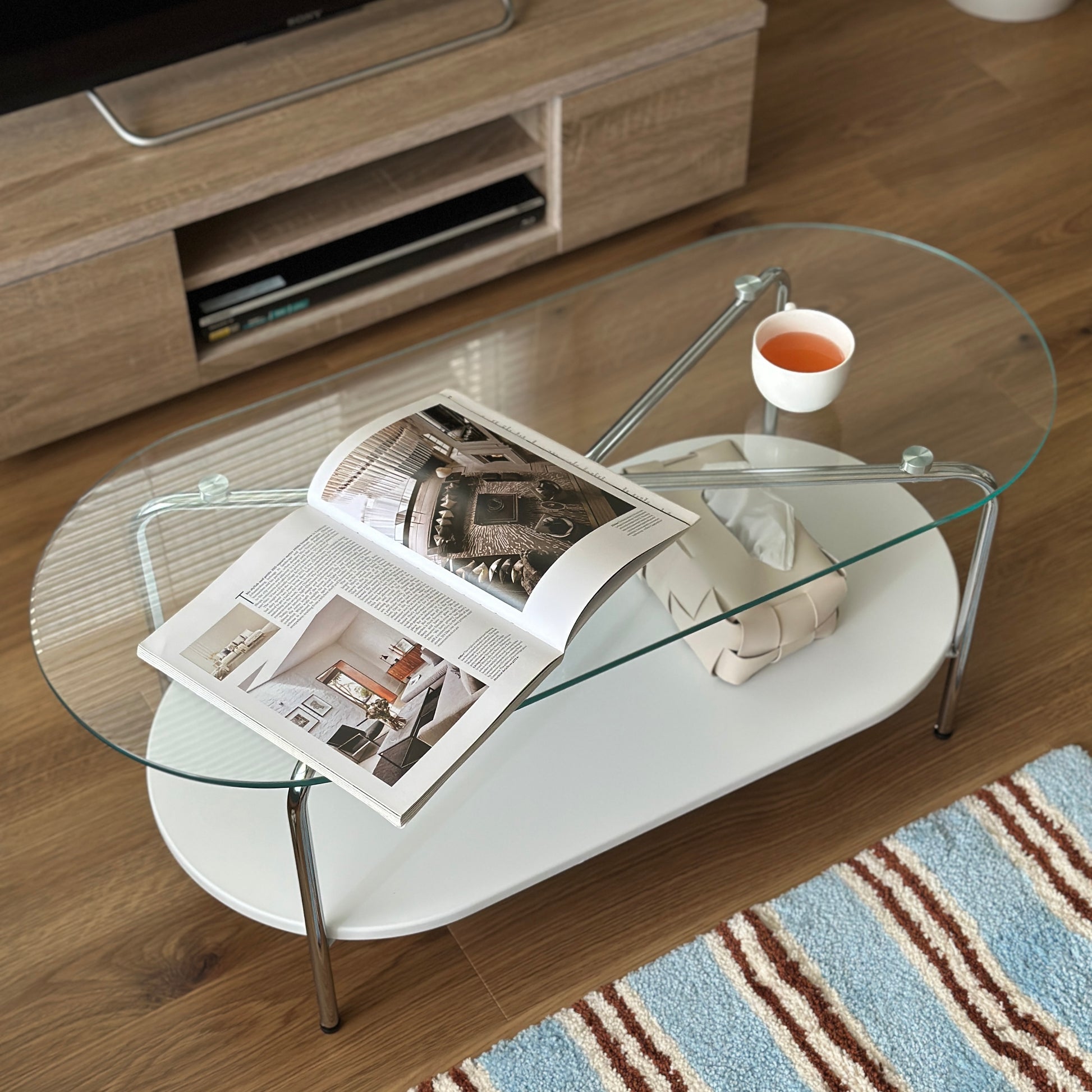 丸みのあるガラス天板のローテーブルの天板上にはコップと雑誌が置かれており、下の棚にはティッシュケースが置かれてある