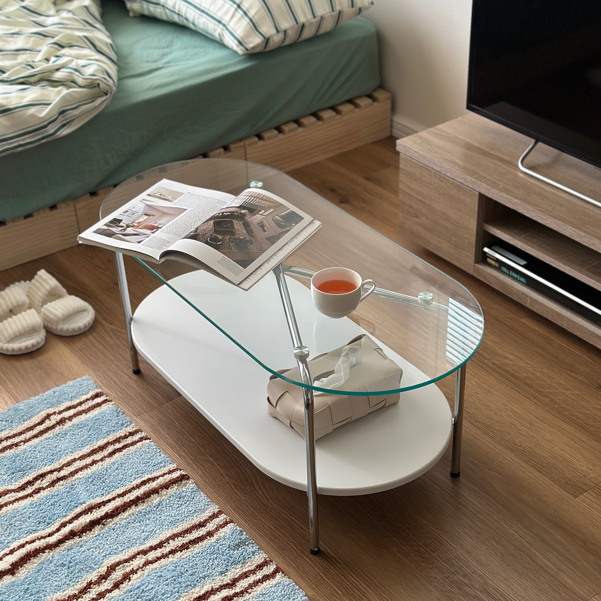 丸みのあるガラス天板のローテーブルの天板上にはコップと雑誌が置かれており、下の棚にはティッシュケースが置かれてある