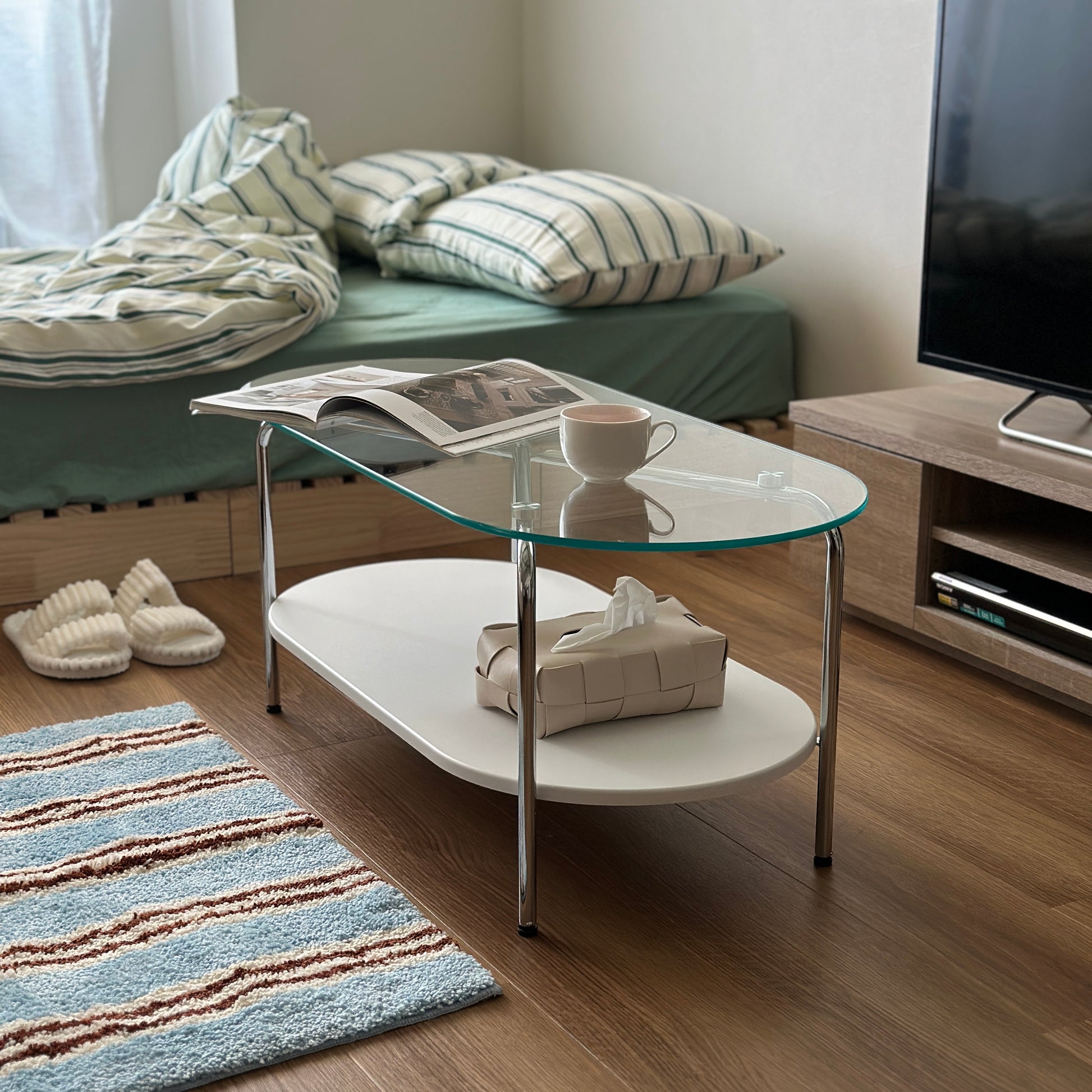 丸みのあるガラス天板のローテーブルの天板上にはコップと雑誌が置かれており、下の棚にはティッシュケースが置かれてある