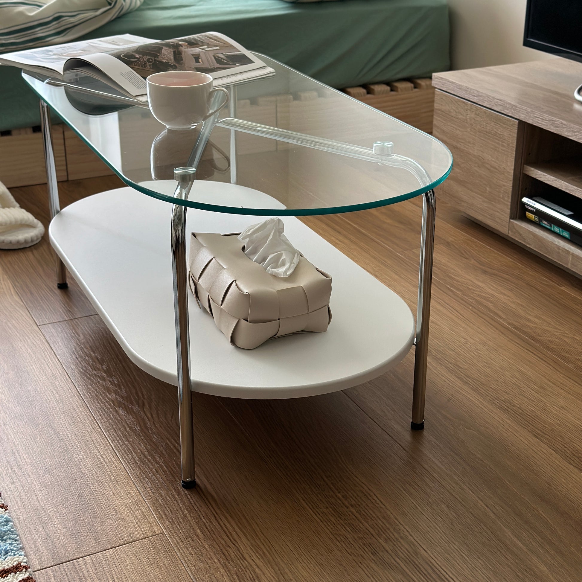丸みのあるガラス天板のローテーブルの天板上にはコップと雑誌が置かれており、下の棚にはティッシュケースが置かれてある